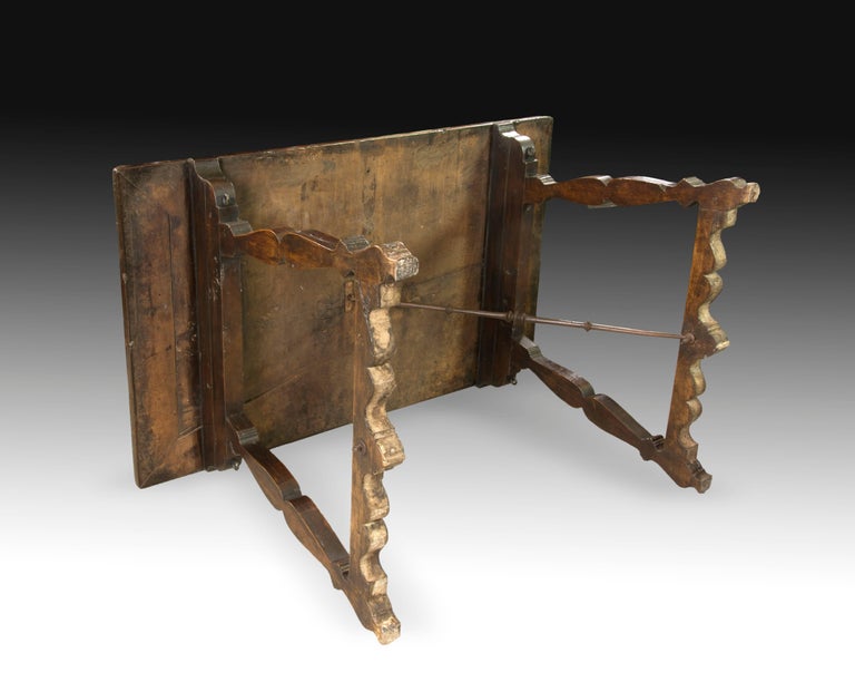 Rectangular table topped with wrought iron fasteners and legs carved with a shape reminiscent of the type known as 