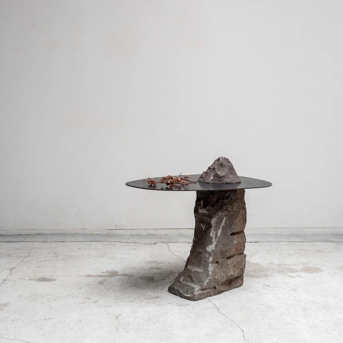 This unique vintage table has been expertly crafted from antique elements, giving it a distinct character. The base is made of a large stone, with a metal plate dividing the piece, its protruding edge serving as the functional tabletop.

The table’s