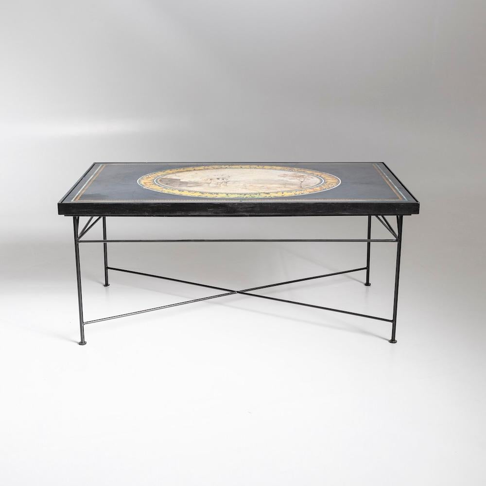 Table rectangulaire en métal laqué noir avec plateau encadré en technique scagliola. La partie supérieure représente un paysage dans un médaillon ovale sur fond bleu.