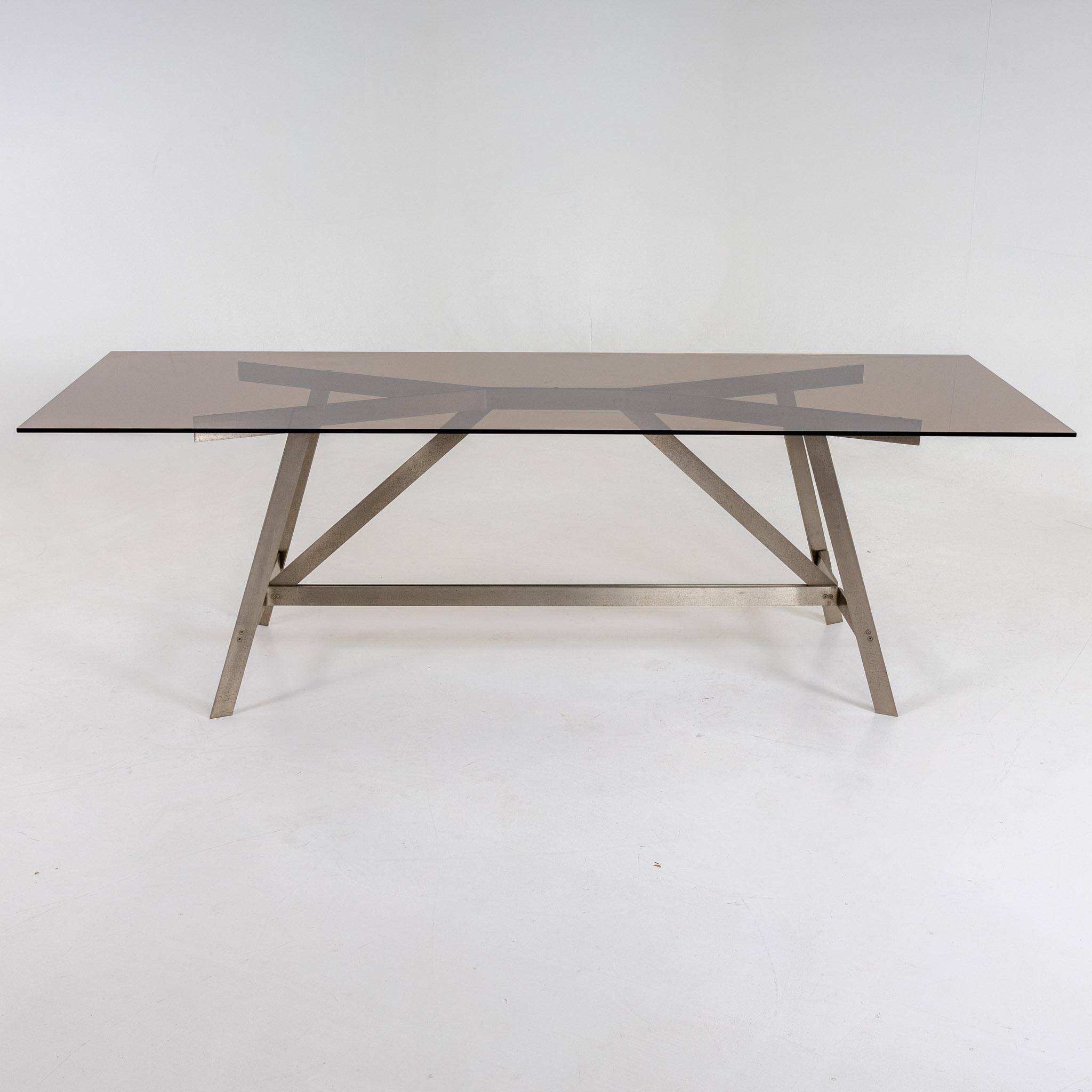 Grande table de salle à manger avec plateau rectangulaire en verre fumé sur structure en acier.