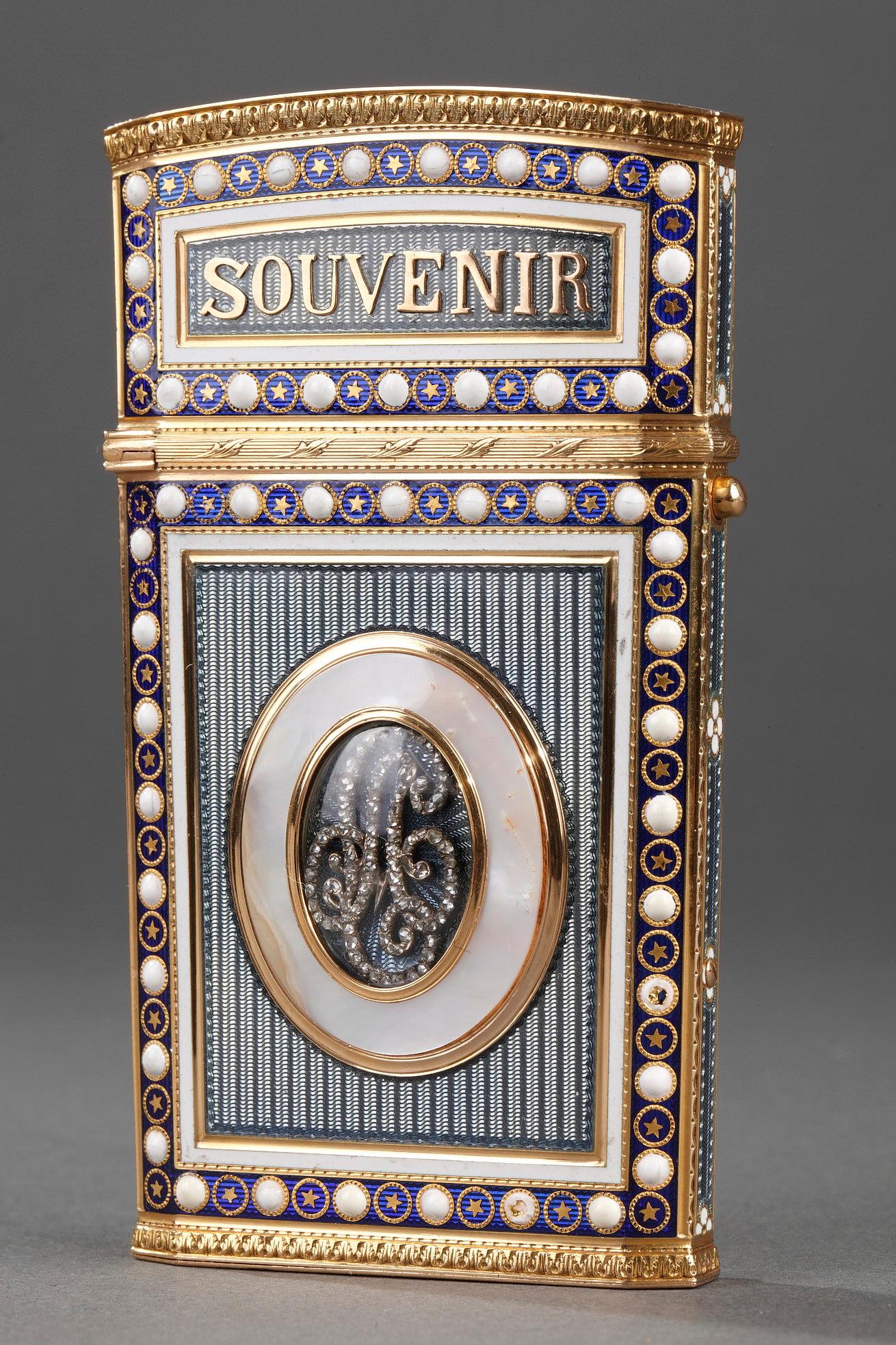 Rectangular writing supplies case with a slightly tapered base and gold mounting. The gold panels of the case are decorated with thin, parallel stripes and overlaid with translucent, lavender blue enamel. A button serves to open the hinged lid which
