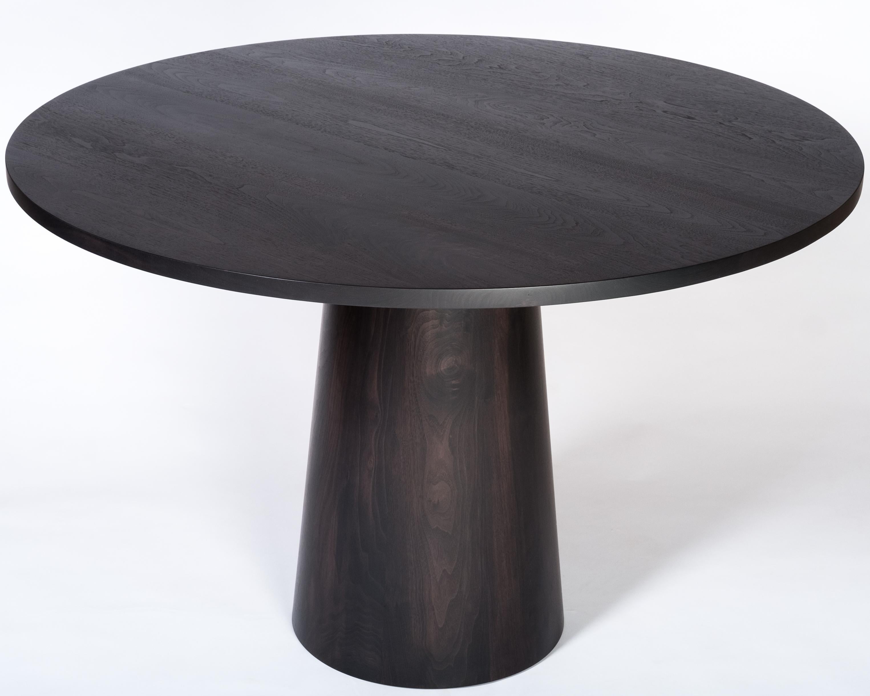 An elegant round dining table with a solid wood base and top. Photos show the table in an oxidized walnut finish which turns the table to a near black yet still allows the beautiful grain and warmth of walnut to come through. Also available in