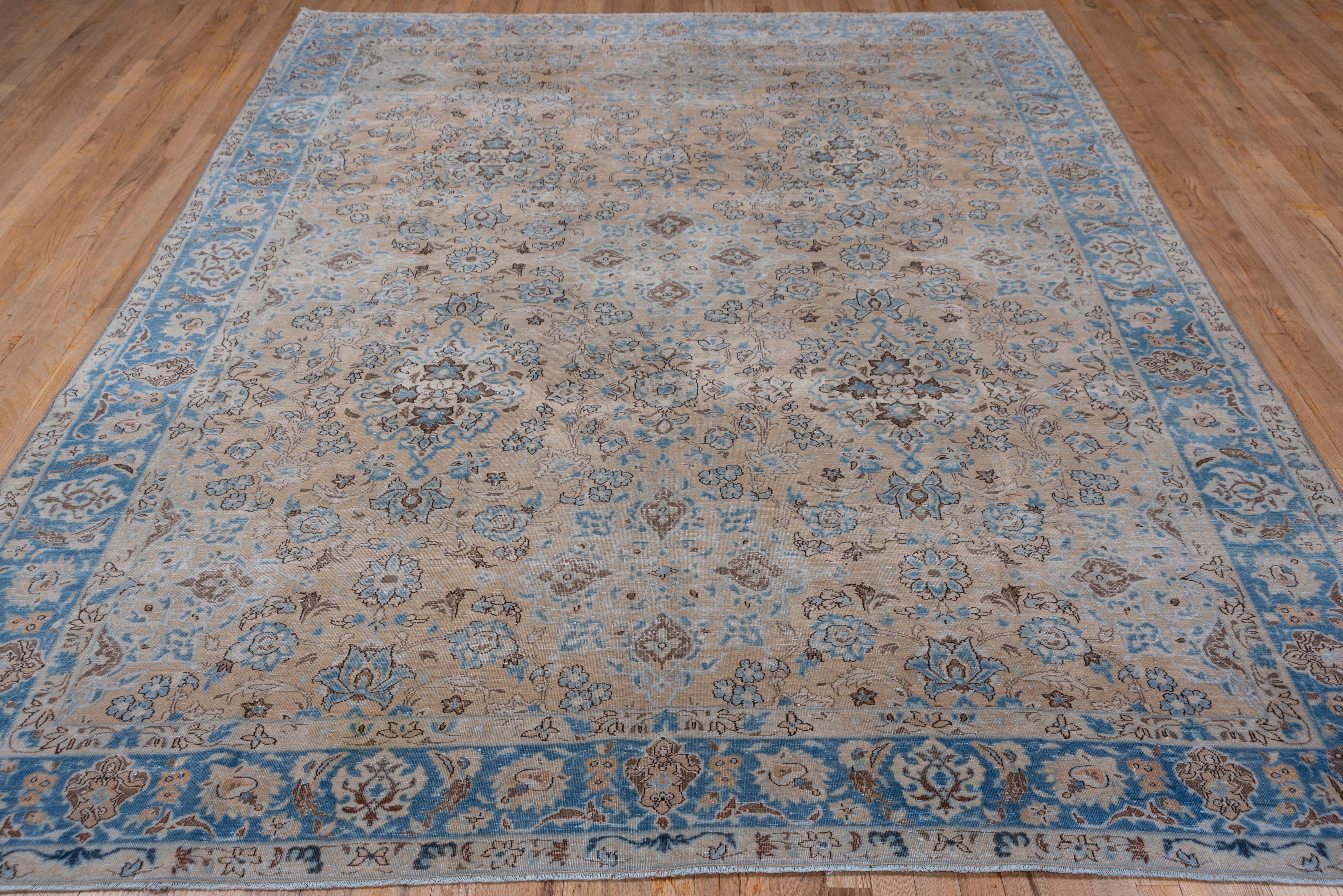 This urban NW Persian carpet features a sandy beige field with a close pattern of palmettes, flower quatrefoils and sinuous leafy vines, accented in powder blue, ivory and red-brown, and framed by a light blue palmette border.