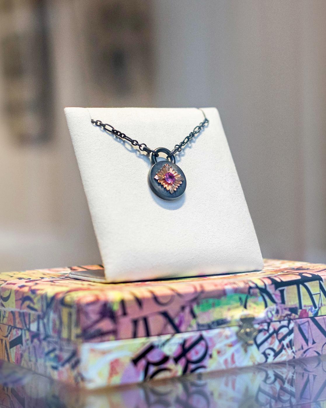Playing with materials. Playing with light. Contrast and color. The Tag necklace embodies the art of composition and eco-creation.

Here, the Tag necklace highlights a ~0.56-carat pink sapphire. The center flower in rose gold rests on a disk in