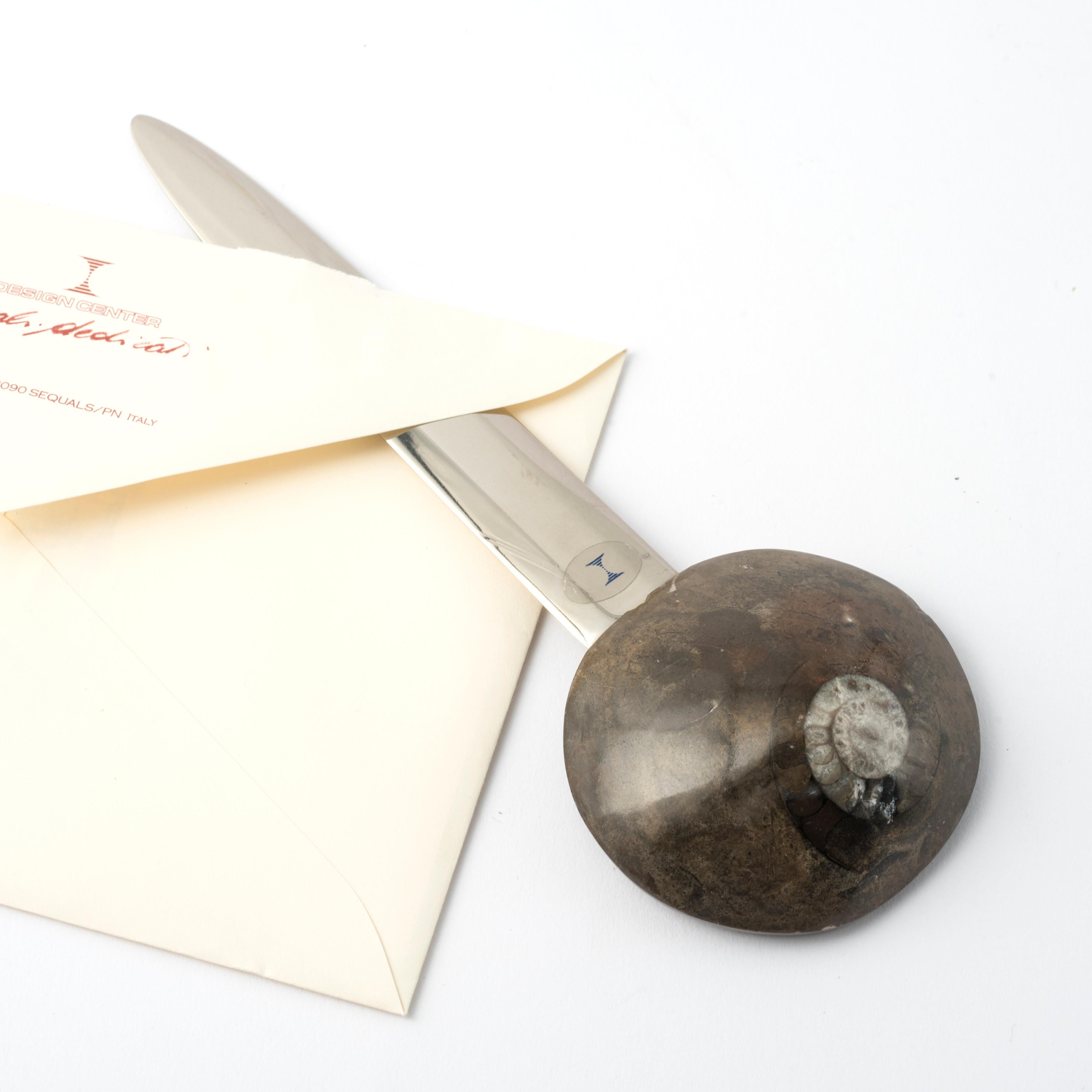 Entdecken Sie den exklusiven Brieföffner aus der Kollektion Fossiline, entworfen von Nino Basso. 
Dieses einzigartige Schreibtisch-Accessoire ist mit einem auffälligen echten Ammoniten verziert, der es zu einem einzigartigen und faszinierenden Stück