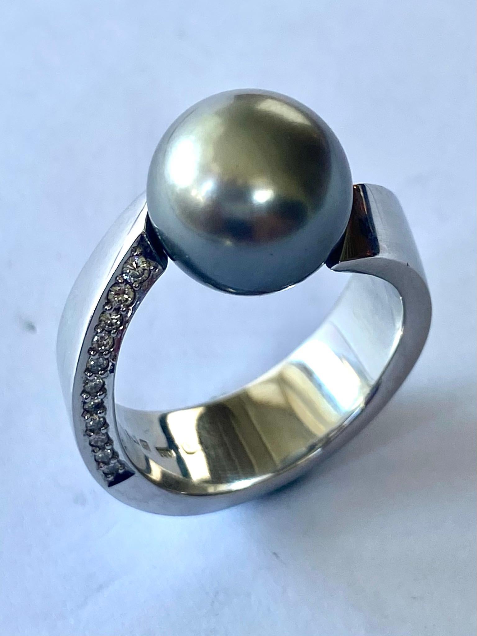 Ein (1) Ring aus 18 Karat Gold, gestempelt 750 und Cs = Schoeffel  Stuttgart Deutschland
Eine (1) sphäroidisch geschliffene Zentralperle (Typ Tahity) von  11.5 -12 mm   = 13,02 ct
Zweiundzwanzig (22) Diamanten im Roudn Briljnat-Schliff = 0,24 ct  VS