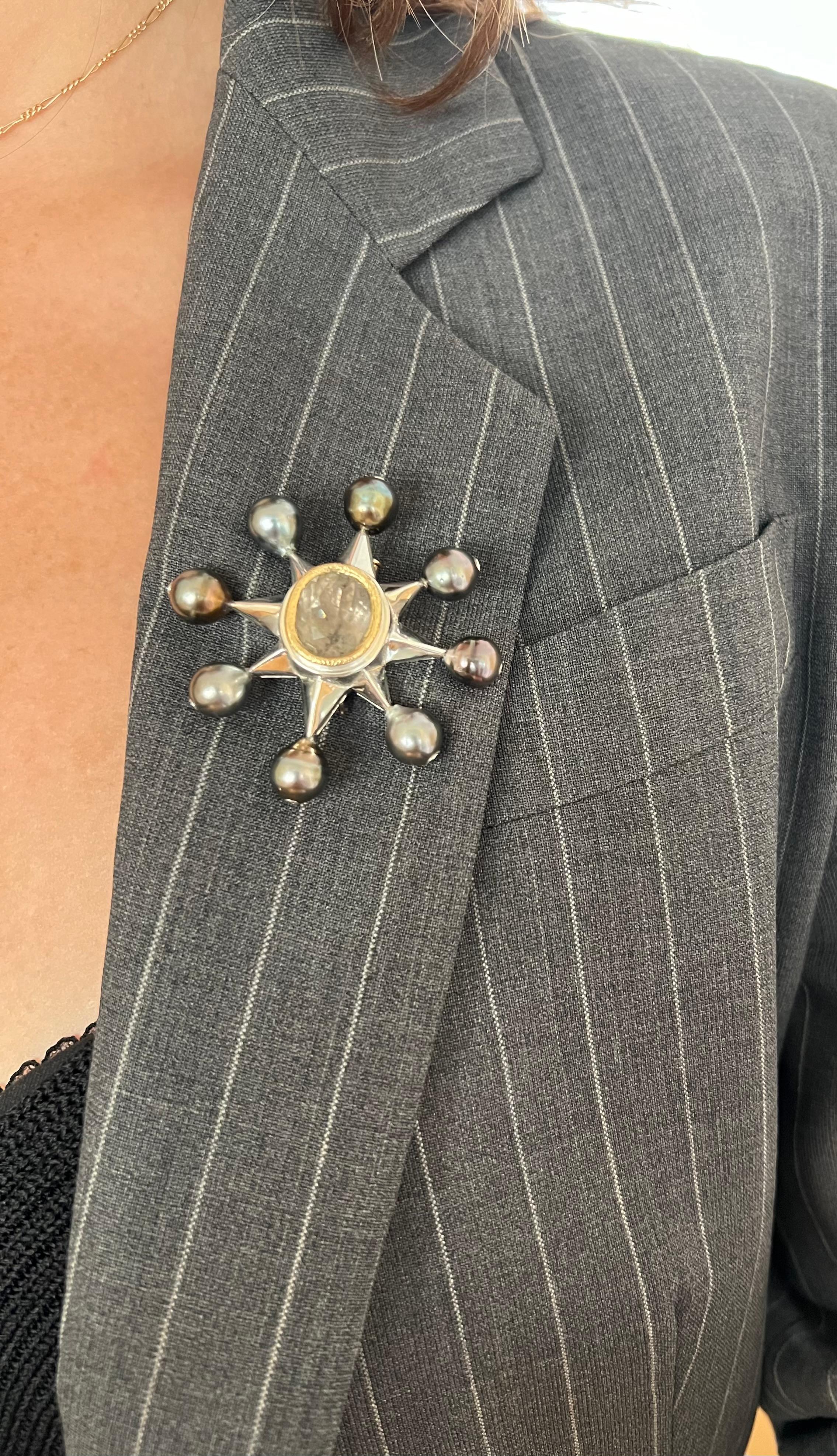 This exquisite modernist one-of-a-kind brooch is a stunning piece of wearable art, meticulously crafted in sterling silver and adorned with luxurious details. At its heart lies an approximately 8.17-carat gray tourmaline, framed by a 20k yellow gold