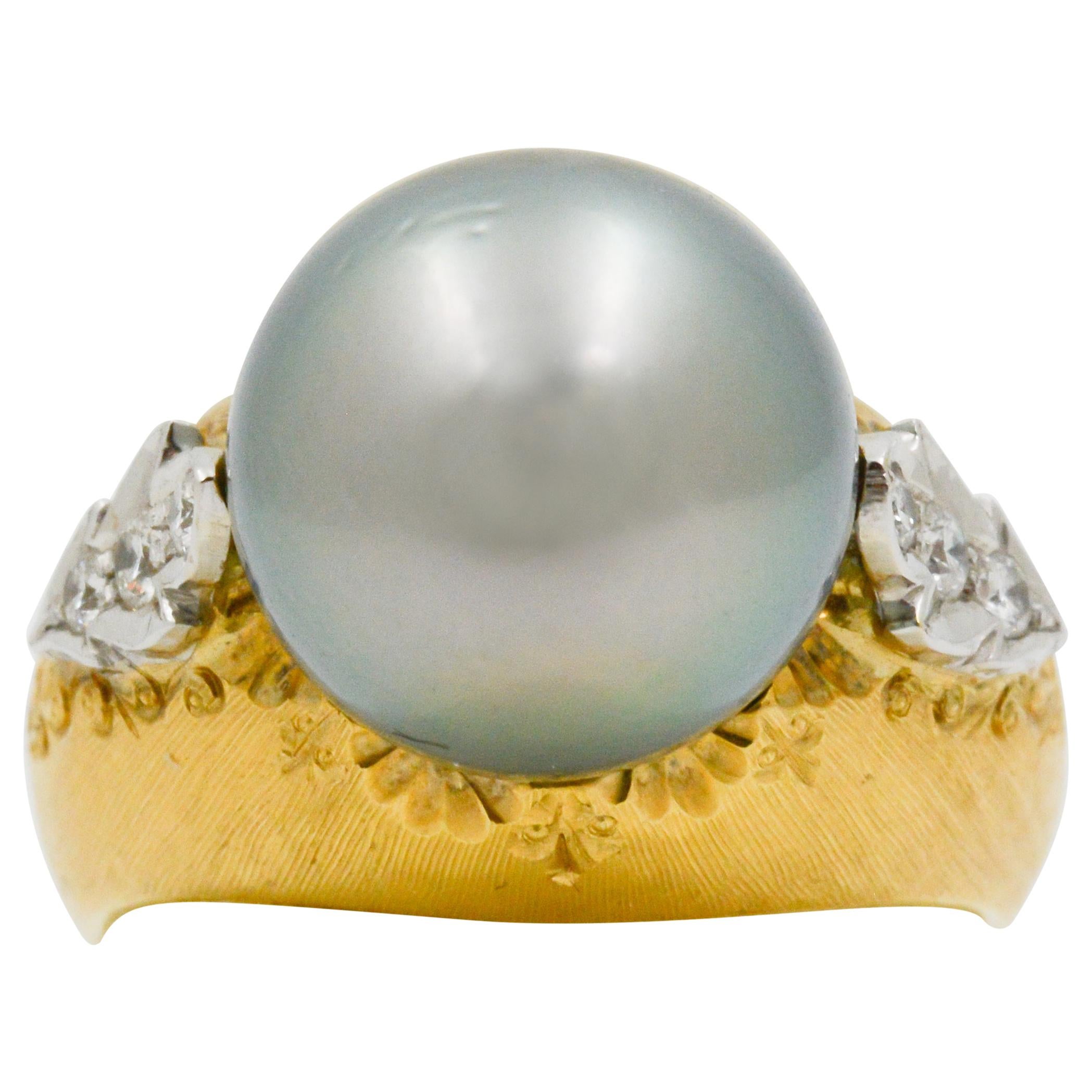 This 18k yellow gold ring features a medium Tahitian grey south sea pearl that is accented by six round brilliant cut diamonds on either side, weighing a total of .14 carats. Surrounding the pearl and diamonds is a scroll work design that adds