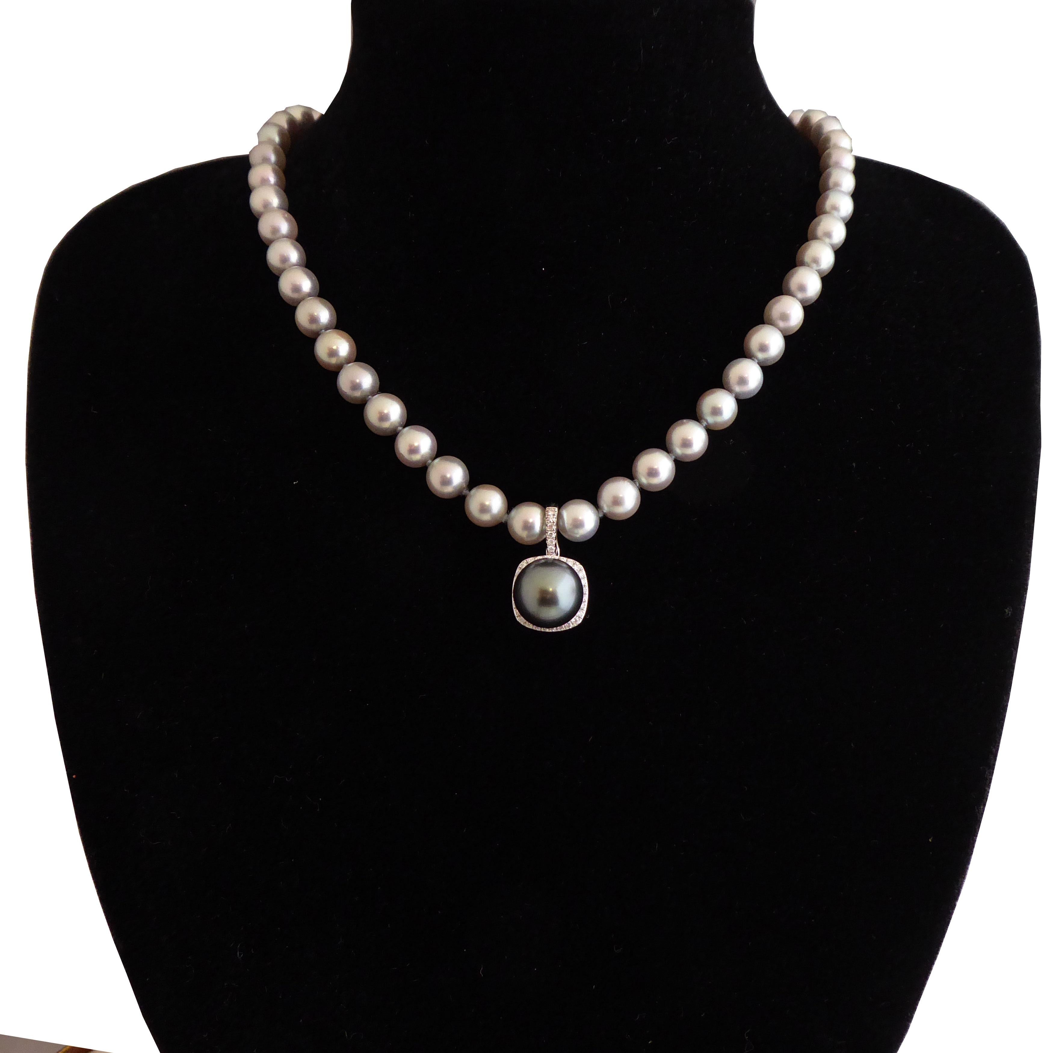 A Tahitian pearl and diamond pendant centrally set with a round Tahitian cultured pearl, measuring 11.50mm-11.60mm, a dark grey colour with a green overtone, and good skin and lustre.  The pearl is peg set into a diamond set, cushion shaped mount