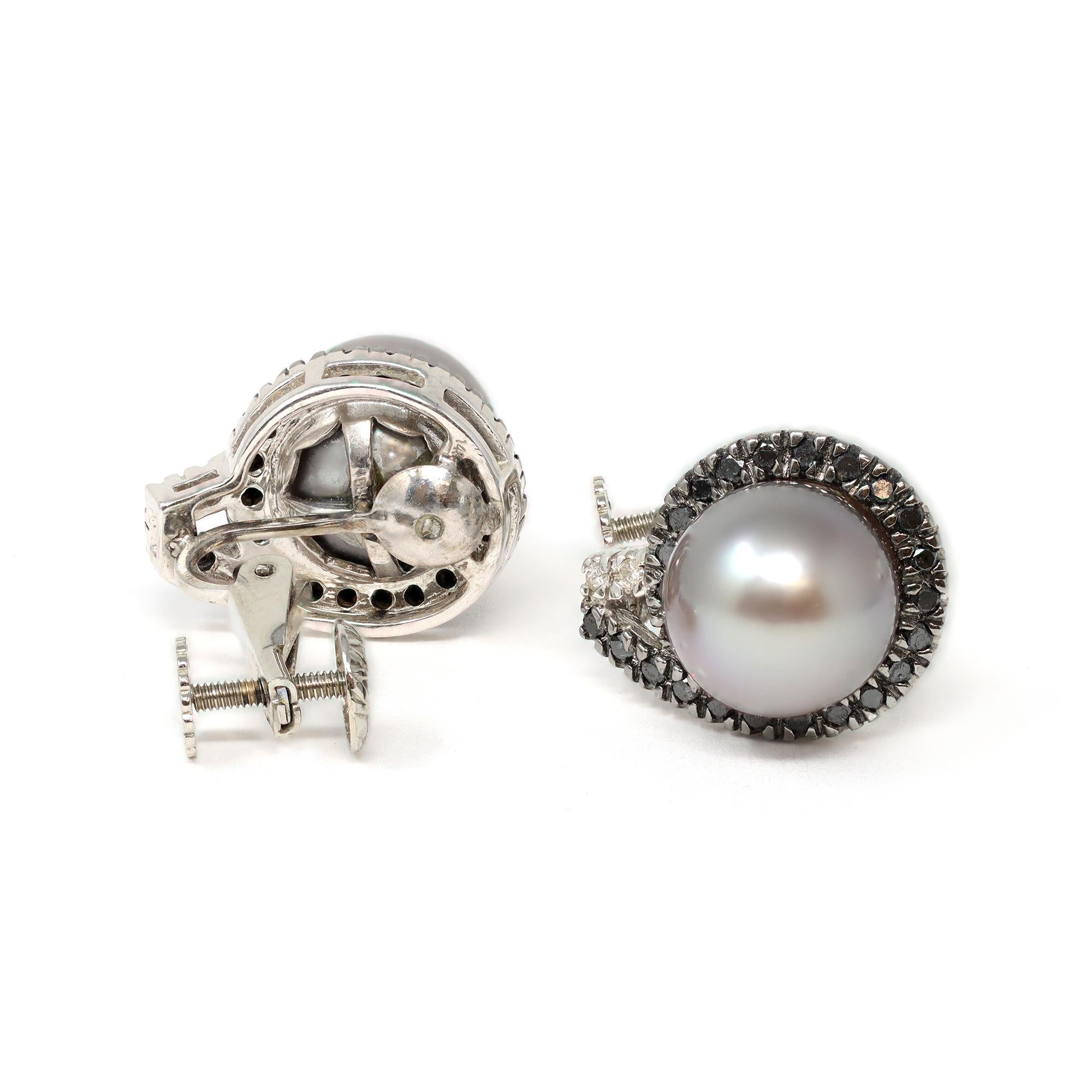 A vintage pair of light grey Tahitian pearl earrings accented by a halo of black diamonds and accent white diamonds. The clip-on earrings circa 1980-90 are set in 14-karat white gold. They have posts and omega-backs. The estimated weight of the