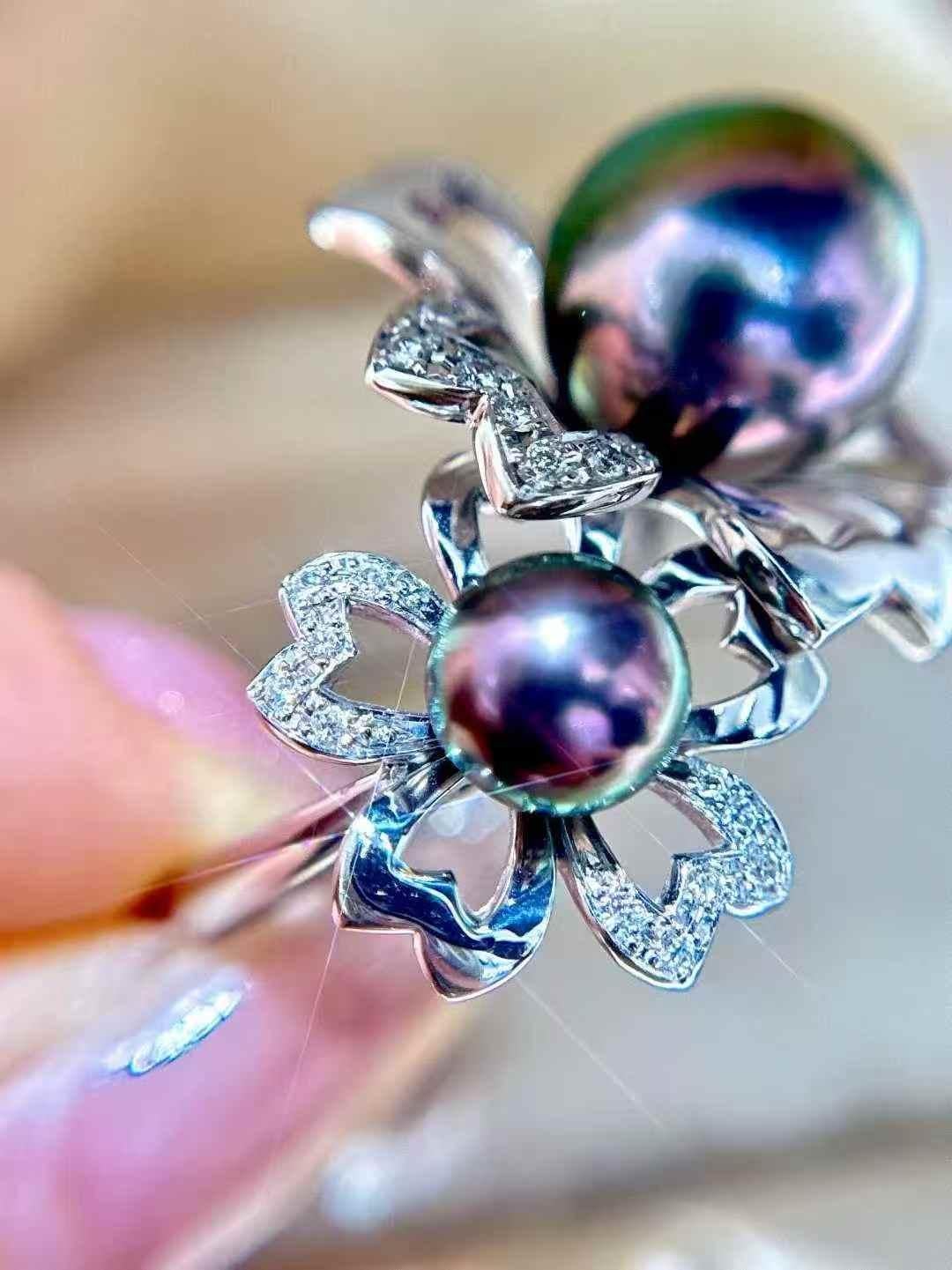 Questo eccezionale anello doppio di perle nere di Tahiti e diamanti presenta una rara accoppiata di perle da 6,8 mm e 11 mm con straordinarie sfumature viola pavone e un caratteristico strato esterno verde con un centro viola vivido. Le perle