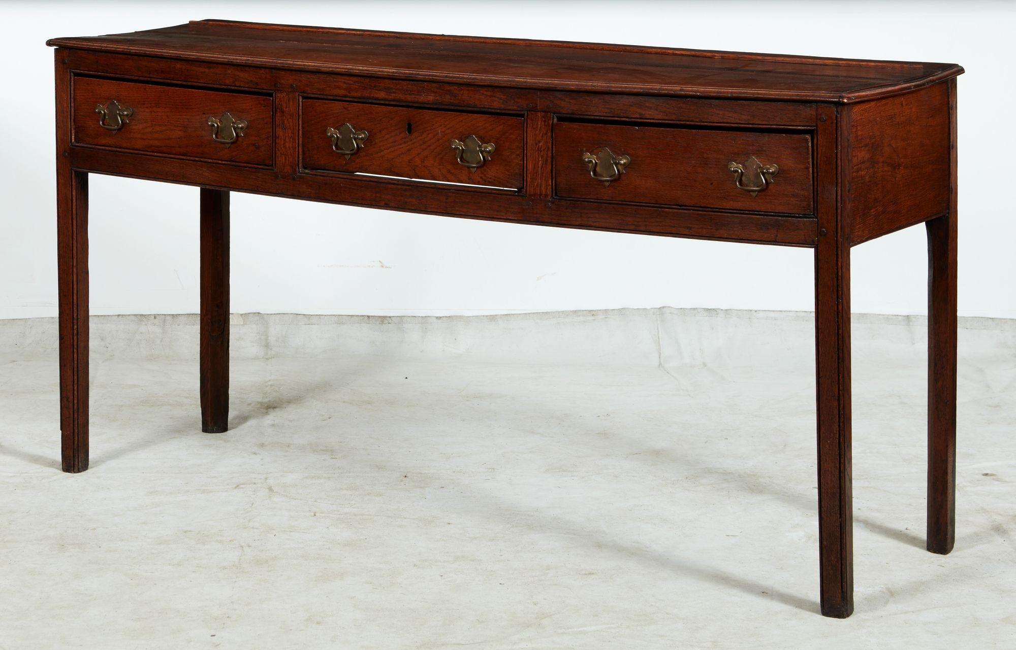 Un comò o credenza del XVIII secolo in rovere con un solido piano a due assi con bordo modellato a pollice su tre lunghi cassetti con doppi tiretti in ottone su piastre posteriori in ottone, con un grembiule dritto e il tutto su gambe a sezione
