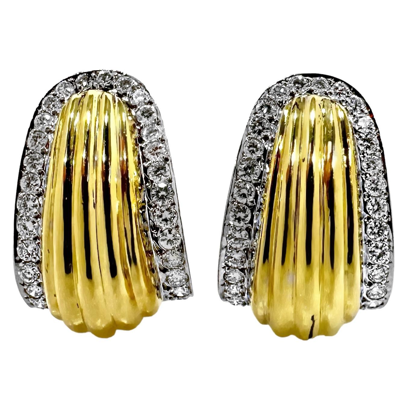 A smart looking pair of 18K yellow gold earrings, centered around a high polished, fluted design. A row of scintillating diamonds set in white gold, move up one side and down the other in a horseshoe shape adding brilliance, while outlining the