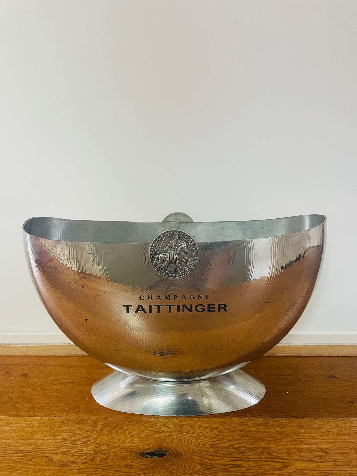 A large Champagne cooler in crescent shape, dimensions 48 x 17 x H30cm, marked Taittinger. The material is pewter (tin), manufactured in France by Orfèvrerie d'Anjou. On the underside marked with the seal of the foundry and 'Etain' in oval tin.