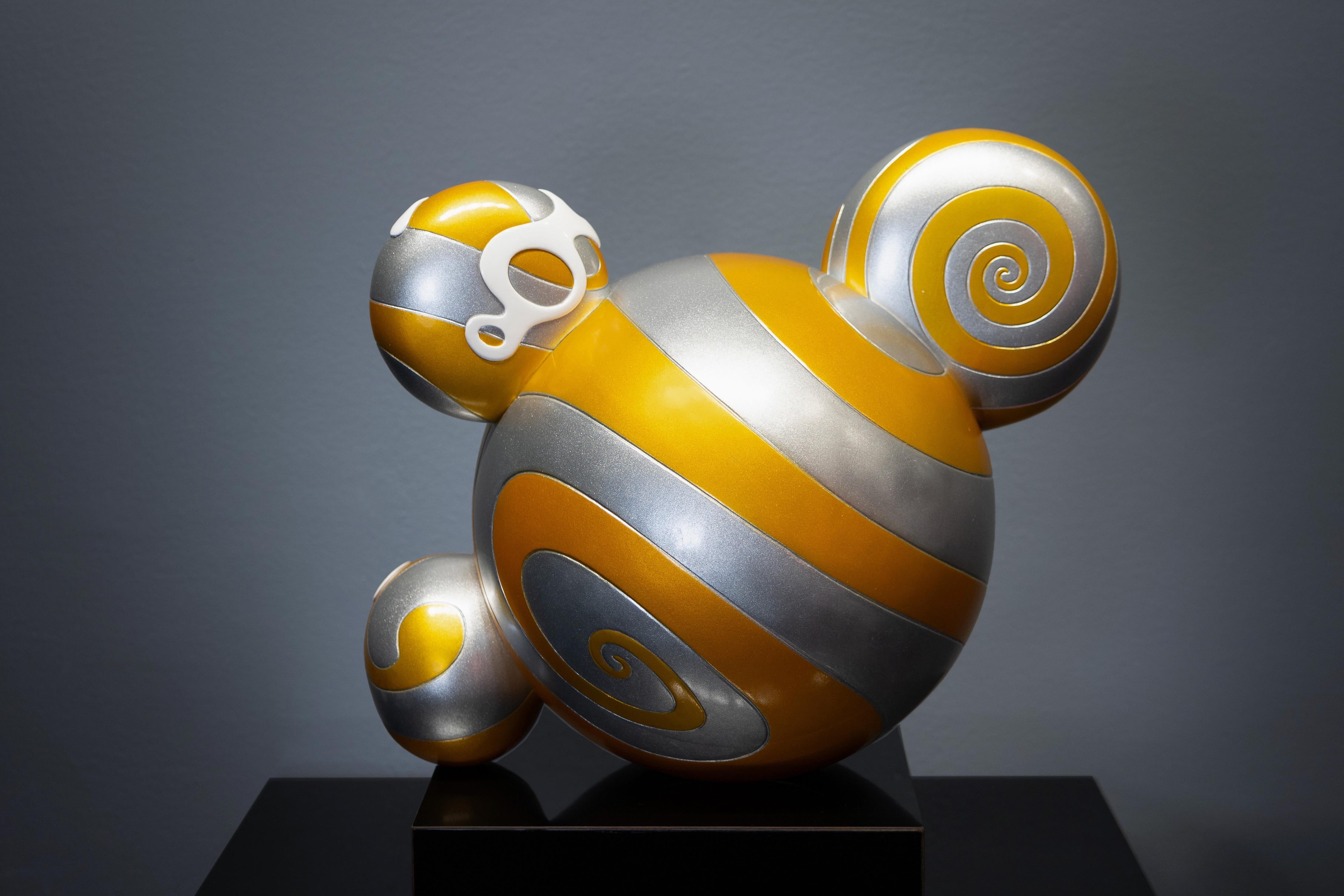 'ComplexCon: Mr. Dob' (Oro), creata da Takashi Murakami nel 2016, è una scultura che fonde l'alta arte, la cultura pop e il commercio. Con Mr. Dob, un personaggio ricorrente dai tratti esagerati e cartooneschi, la scultura è resa in oro brillante,