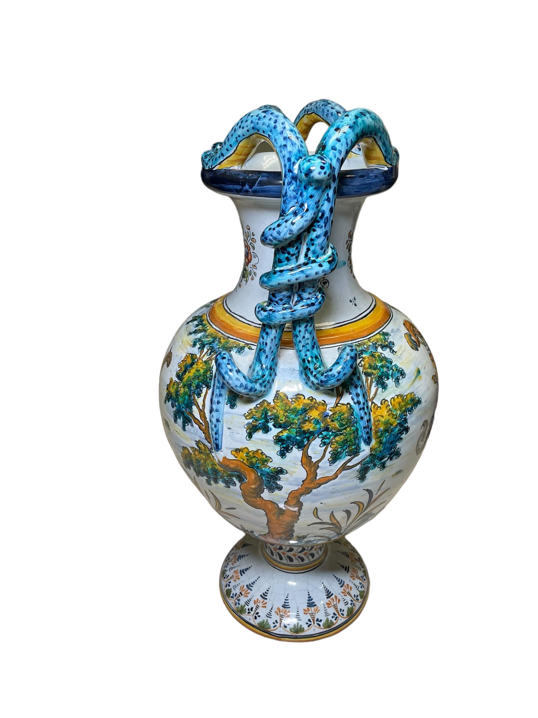 Questo è un vaso ad anfora in maiolica di Talavera. Raffigura un'anfora dipinta a mano con uno sfondo bianco che mostra nella parte anteriore una scena di un gentiluomo spagnolo a cavallo e nella parte posteriore una scena di una capra di montagna.