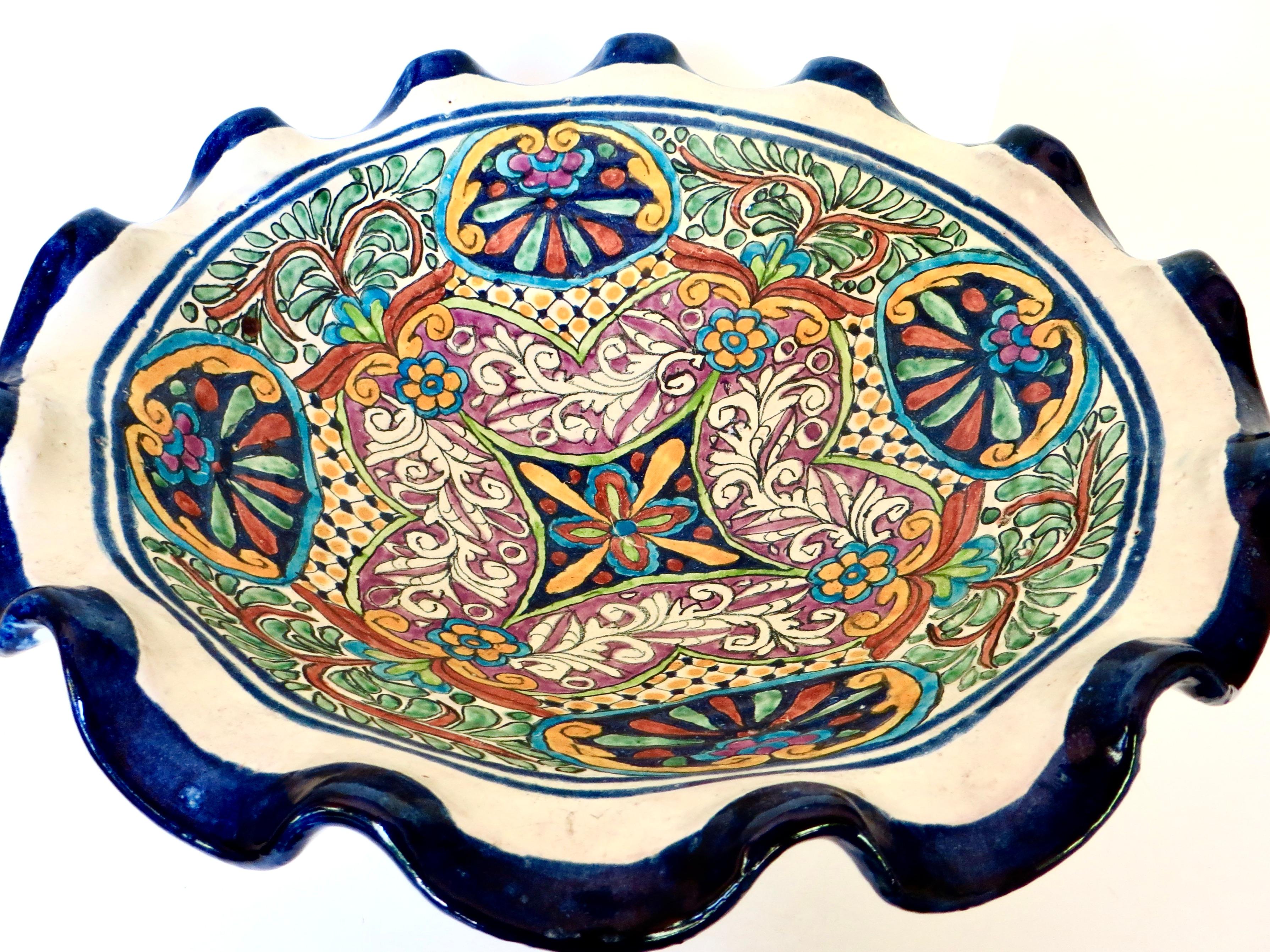 Bellissima fruttiera messicana di grandi dimensioni con influenza Talavera del periodo coloniale spagnolo; disegno floreale multiplo dipinto a mano nei colori verde, ruggine, giallo pallido, nero, malva bianca e blu intenso. La superficie smaltata è