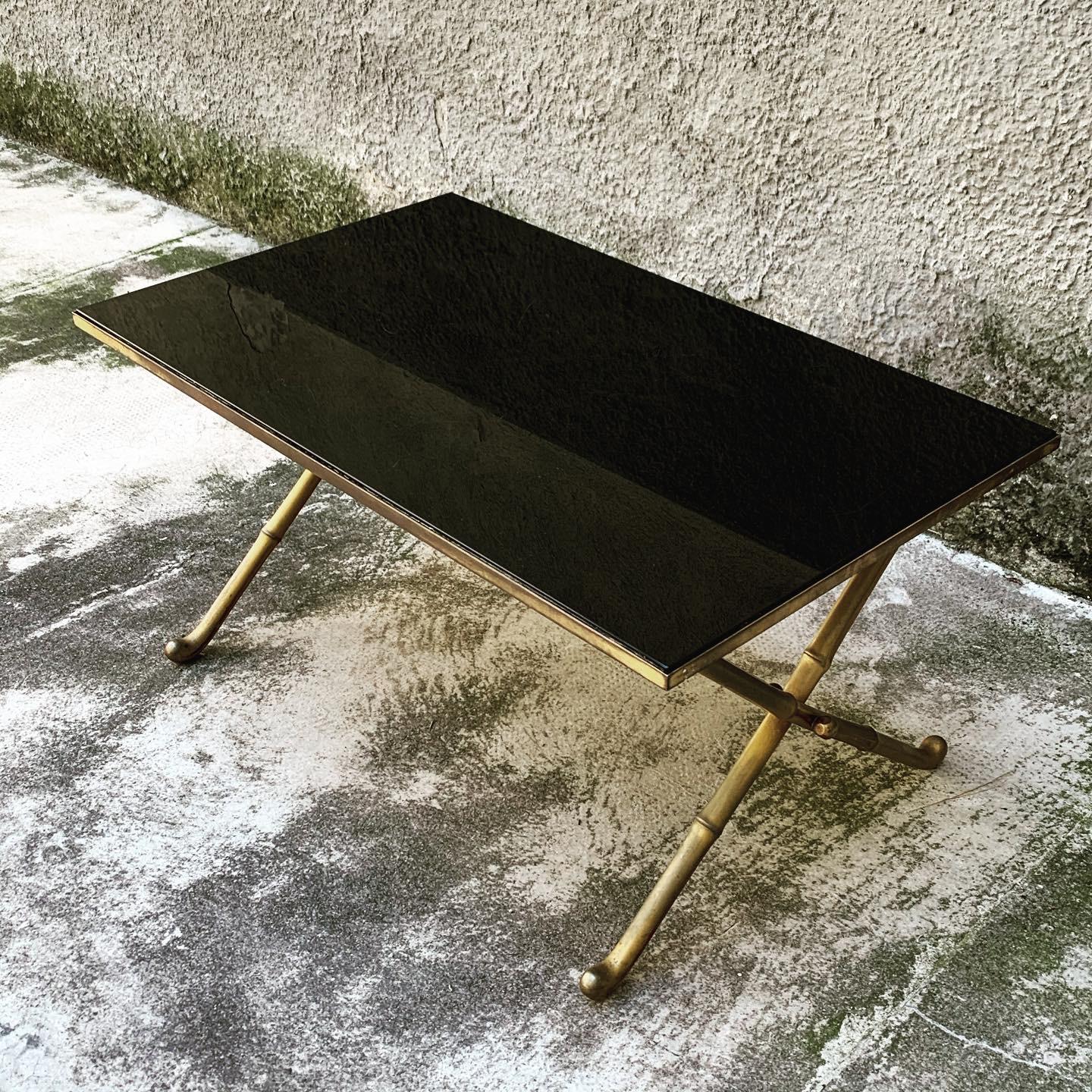 Small brass coffee table with black opaline glass top and X-shaped cross legs, from the mid-20th century period.
The glass top has several surface scratches.
