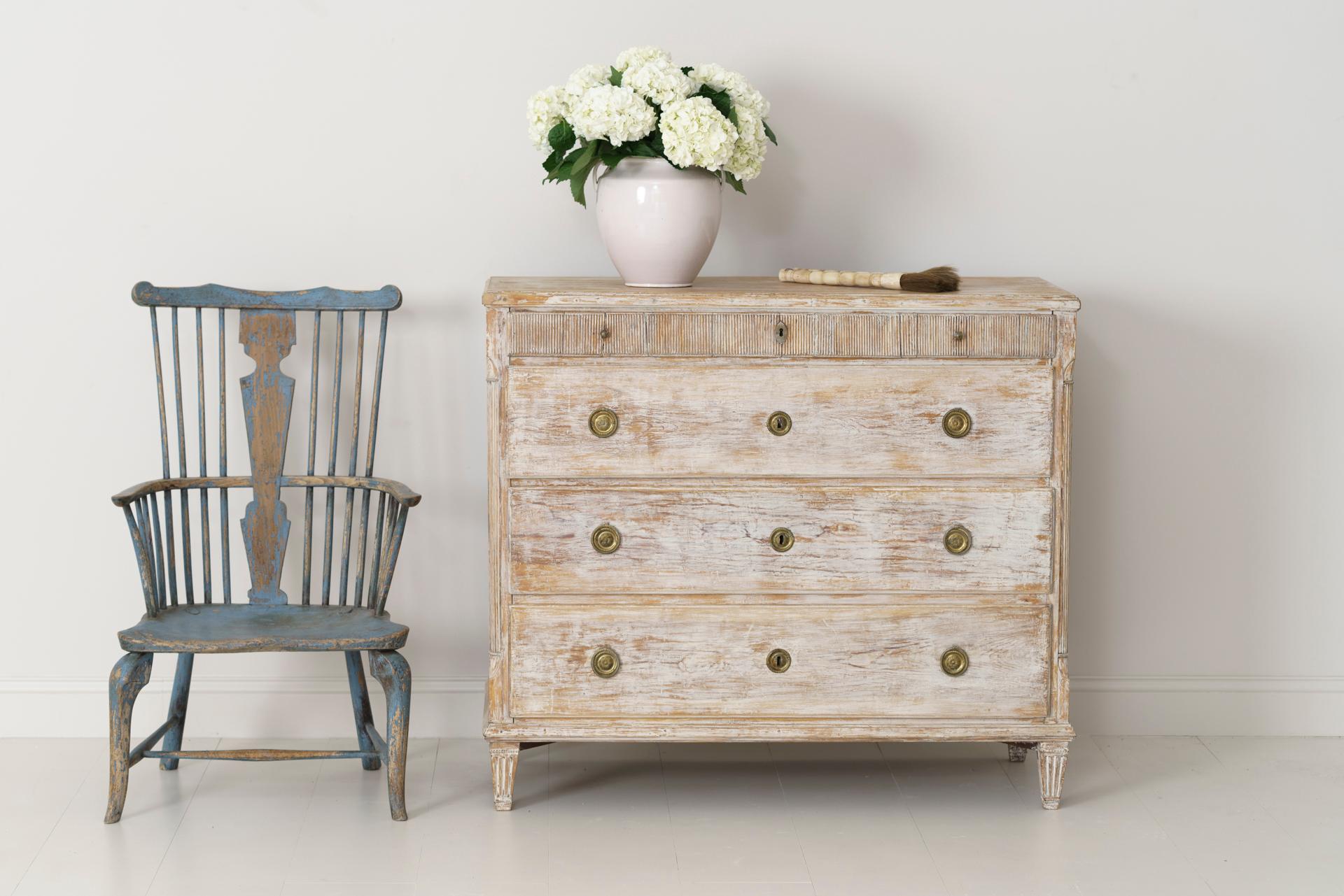 An 18th century Swedish commode from the Gustavian period, dry scraped back to reveal the original white paint and natural wood surface. This tall commode has three deep drawers with one small, reeded drawer and reeded corner columns, raised upon