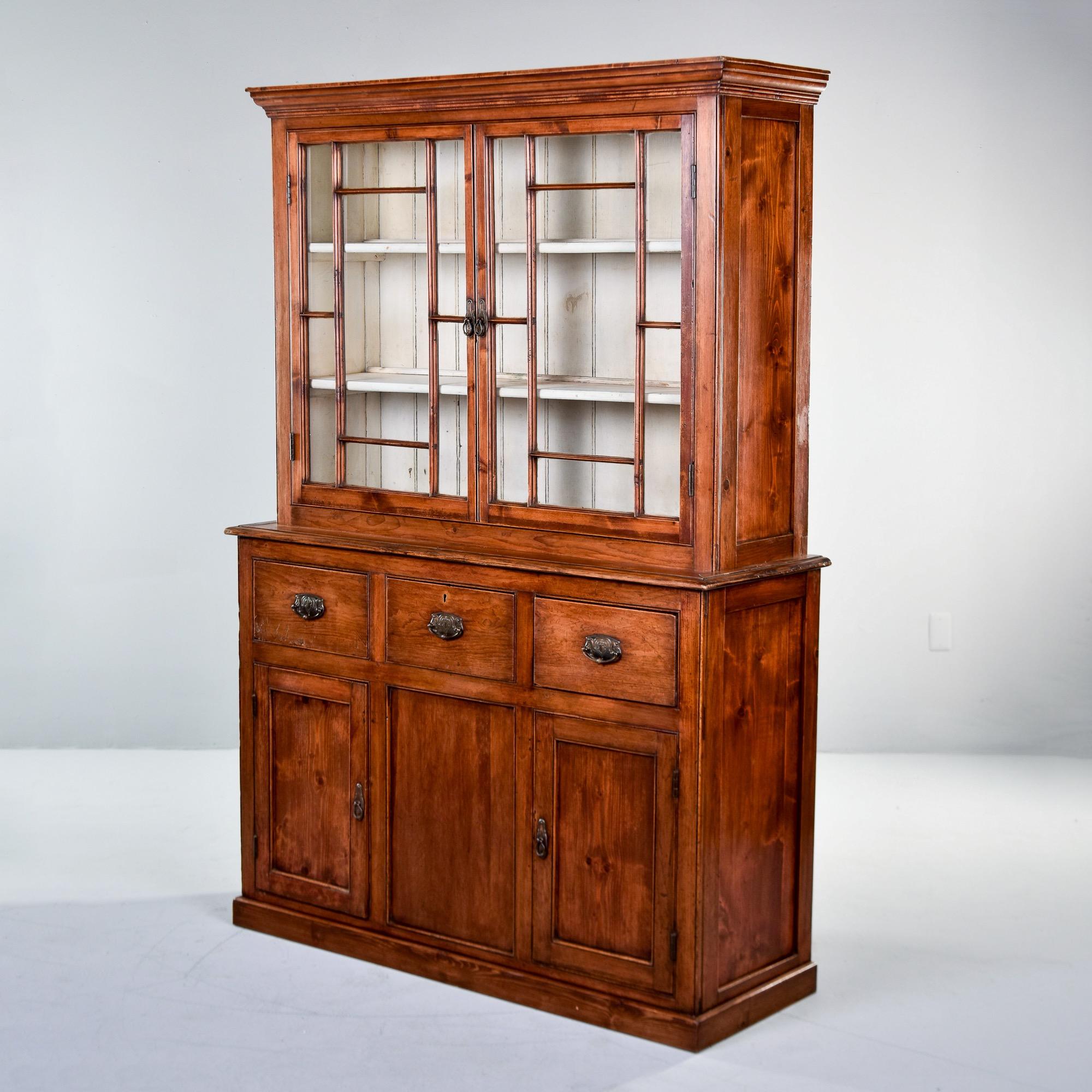 Found in England, this pine cupboard dates from the 1860s. Base has three functional drawers with original hardware over two hinged doors at the bottom that open to storage with a single interior shelf. Top has glass fronted doors that open to white