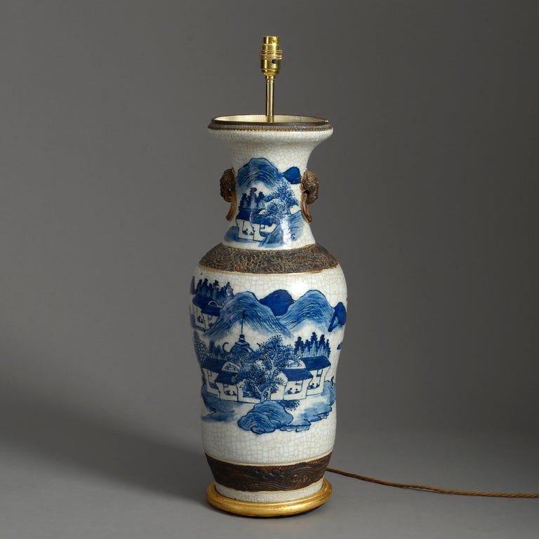 A large scale blue and white glazed crackleware vase, with bronzed collar, base and lion mask handles. Now mounted upon a hand-turned giltwood base as a lamp.

Dimensions refer to vase and gilded base only

Shade not included.