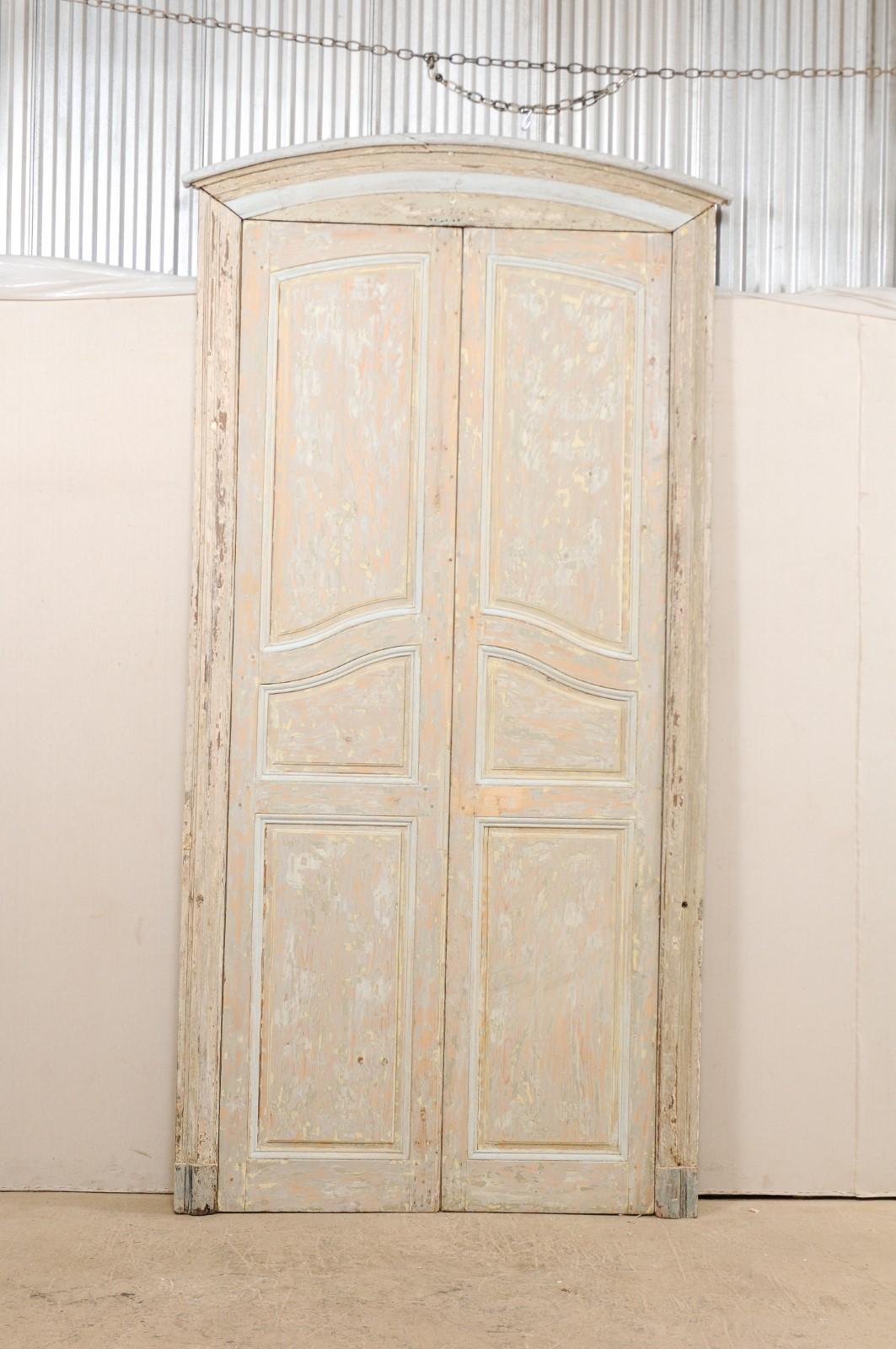 This is an impressive pair of tall 19th century French doors with their original casing and subtle arched crest top. This pair of tall antique doors from France with curvy raised panels and original finish are framed within their original casing,