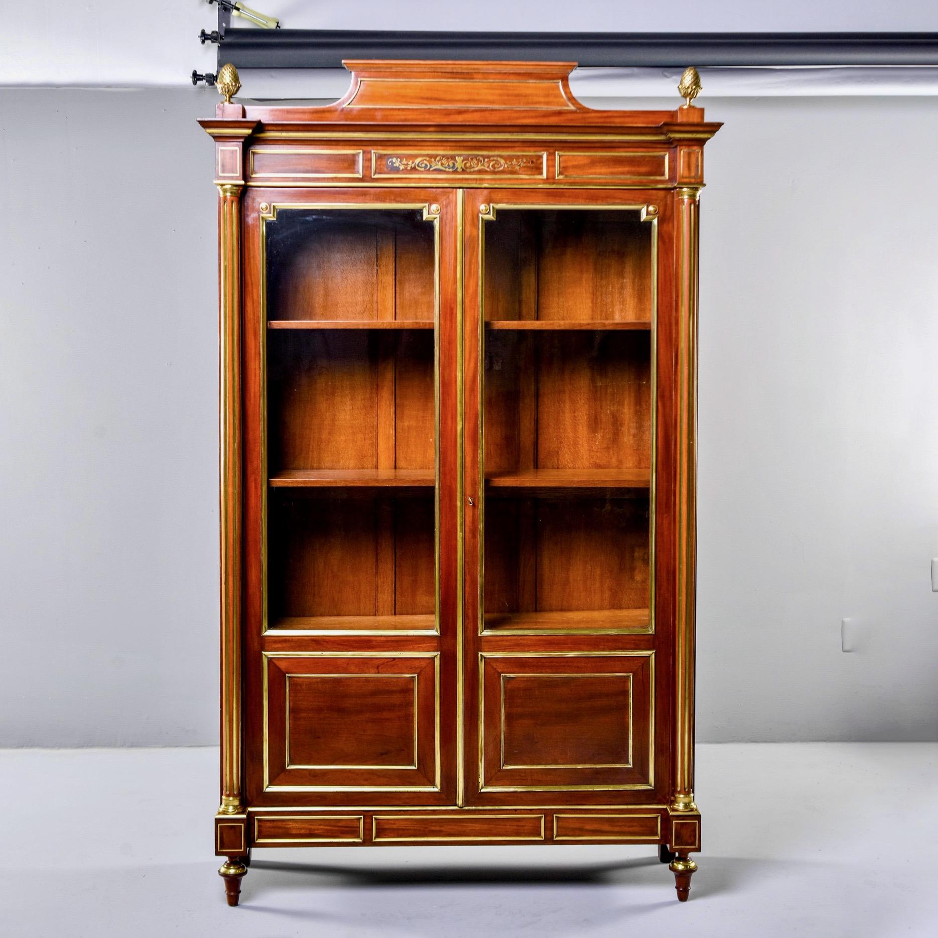 Tall French Louis XVI style vitrine in mahogany with extensive brass detailing, circa 1860s. Two hinged glass front doors open to a compartment with three internal shelves and functional key. Doors have decorative brass trim, and more decorative