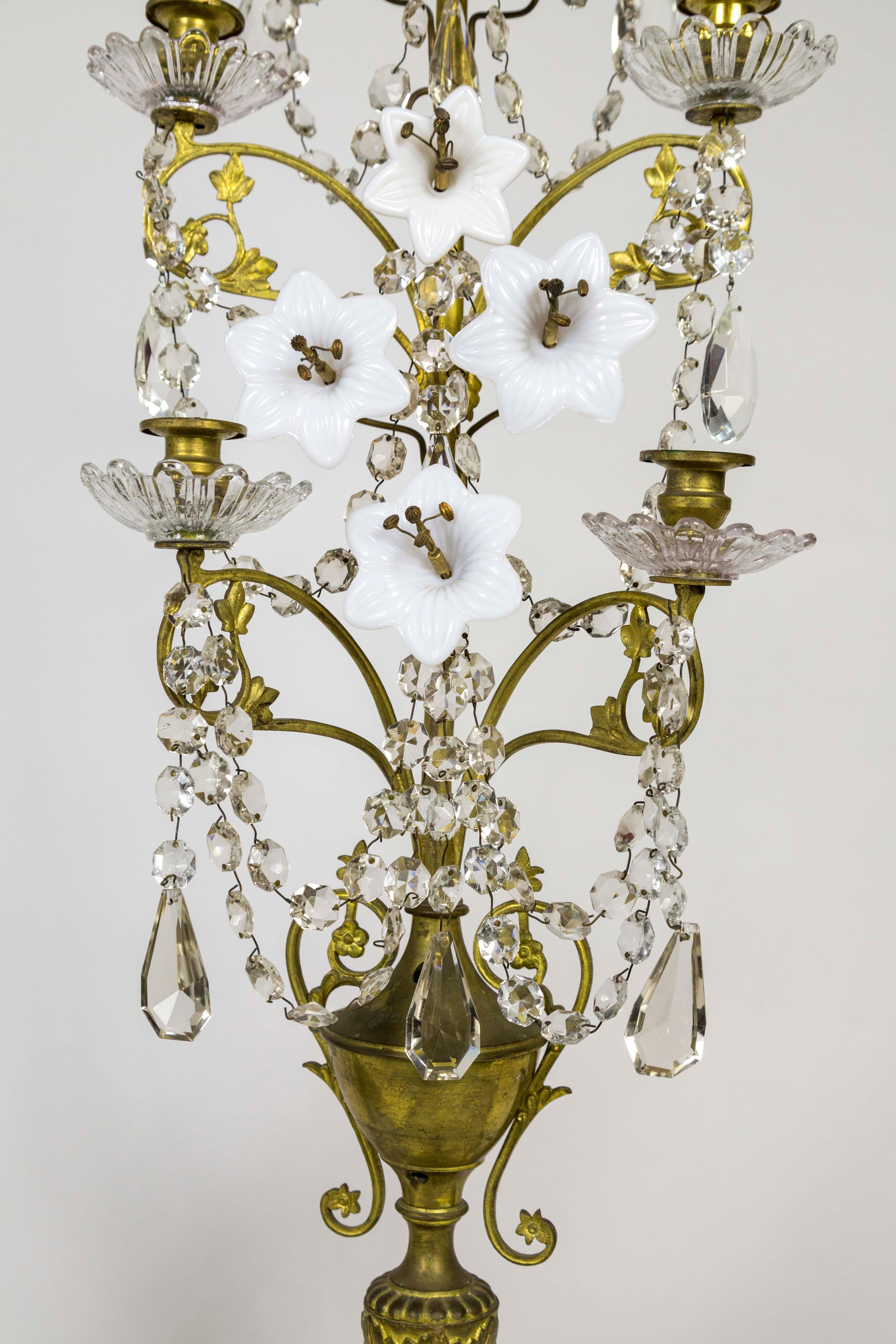 A pair of tall, narrow, multi-tier, brass candelabra with ornate decoration - brass scrolls, milk glass lilies; large, faceted crystal almonds and octagon garlands; an elaborate, urn tripod, base with cherub faces and leaves; glass bobeches.