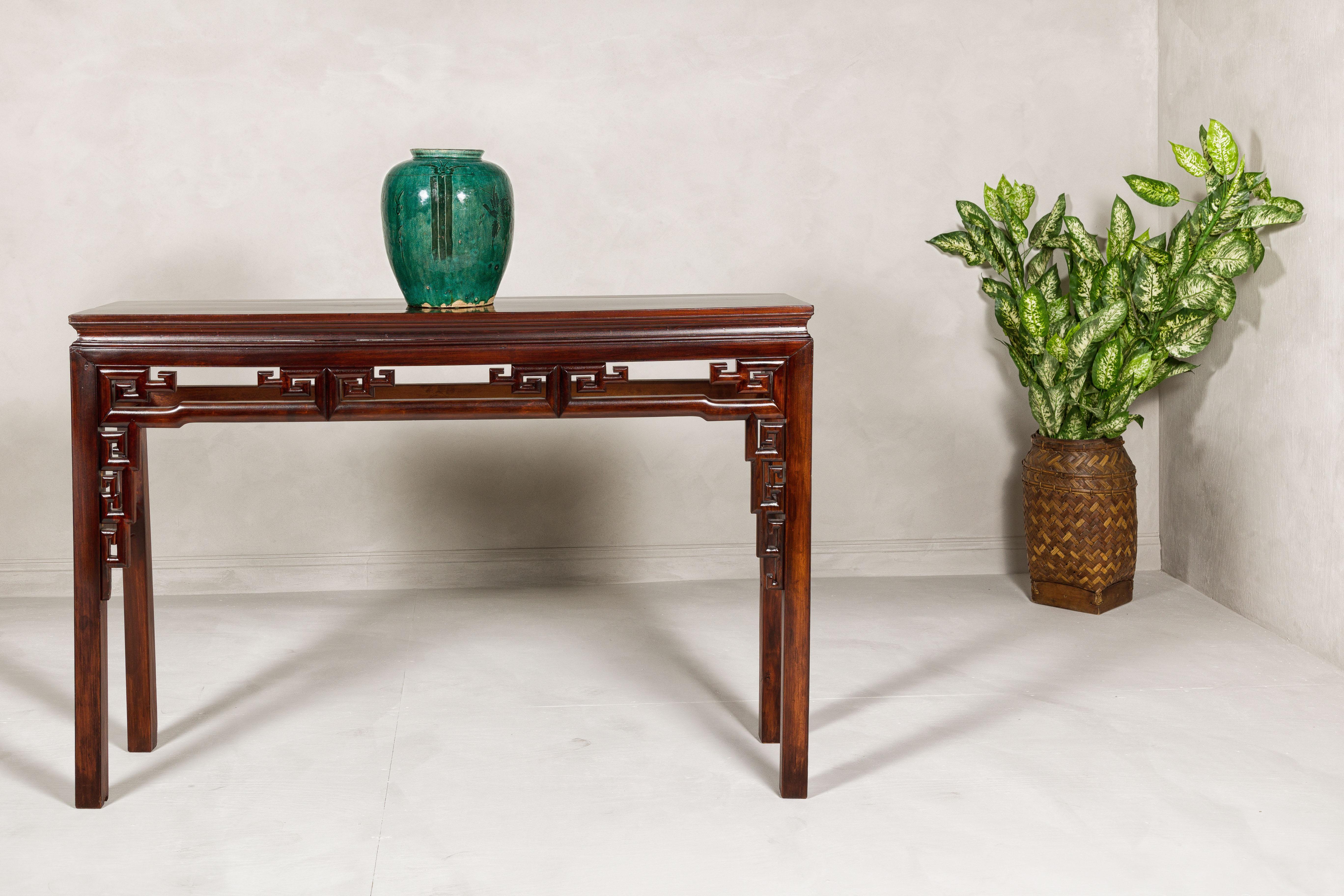A vintage Chinese carved altar or scroll table from the mid 20th century with meander carved apron and lateral humpback stretchers. This mid-20th century vintage Chinese altar or scroll table has been beautifully restored, showcasing a reddish-brown