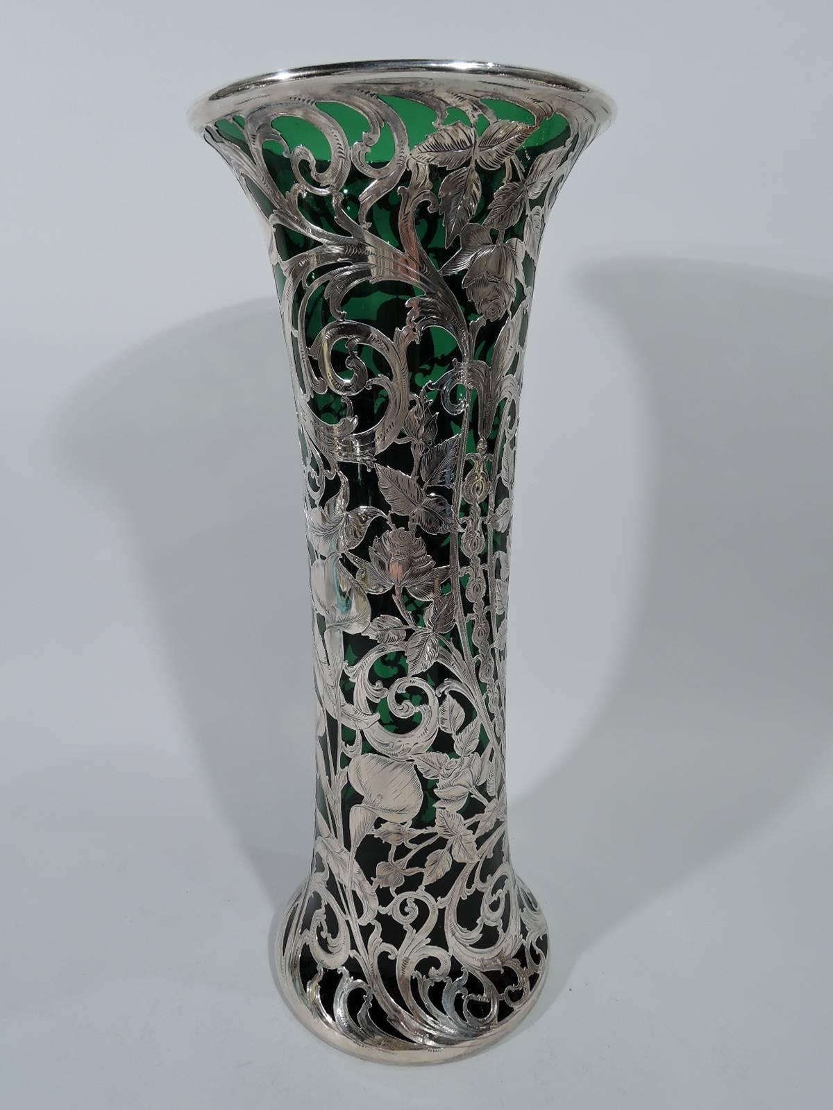 Tall Art Nouveau emerald glass vase with silver overlay. Made by Alvin in Providence. Cylindrical with flared rim and spread foot. Dense and engraved foliate scrolls and flowers. A fluid and dynamic design with lush blooms. Scrolled cartouche