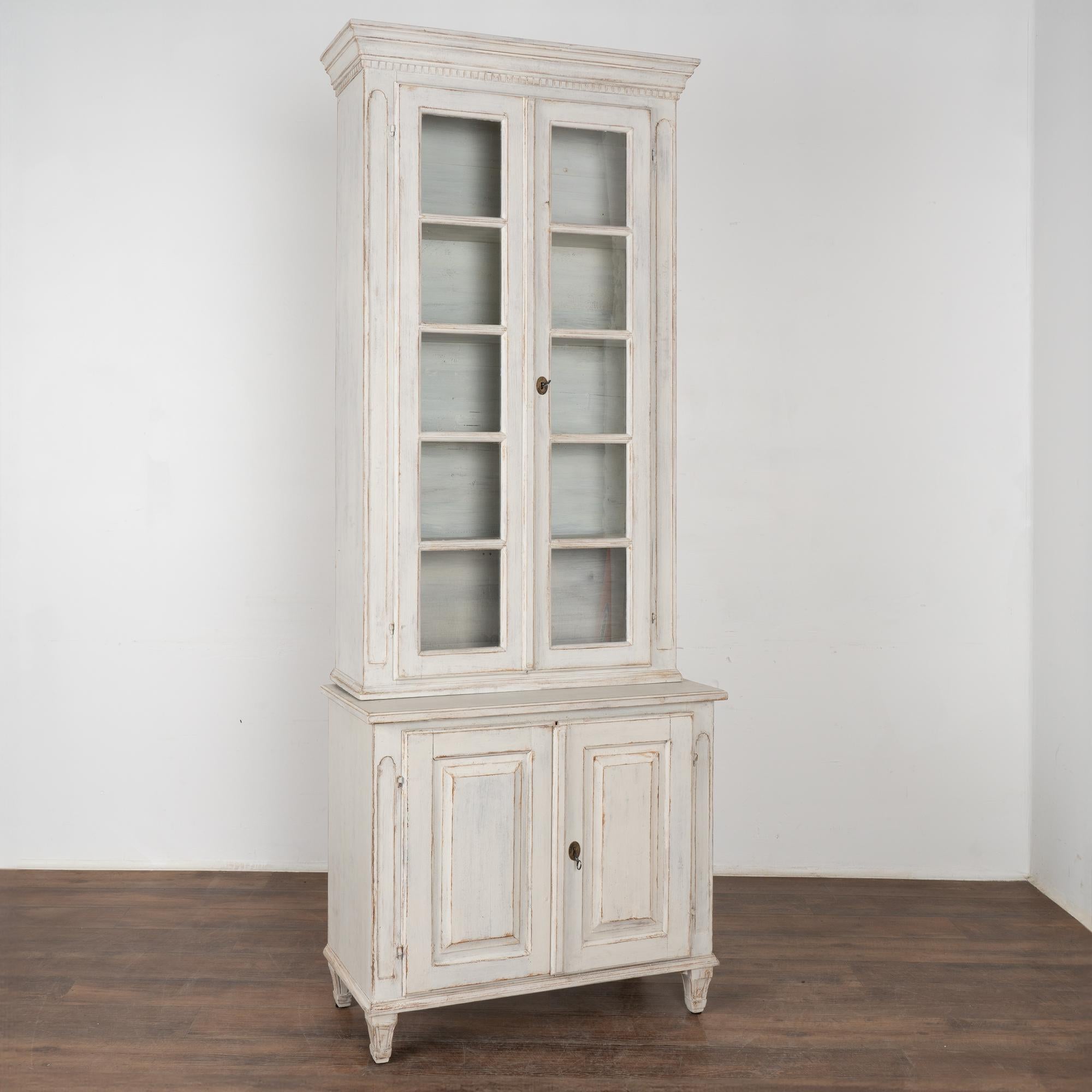 Delightful tall and narrow white painted pine bookcase built in two sections for easier installation. Stands just under 8' tall.
Dentil molding along crown and simple carved details along vertical sides of doors.
Restored, later professionally