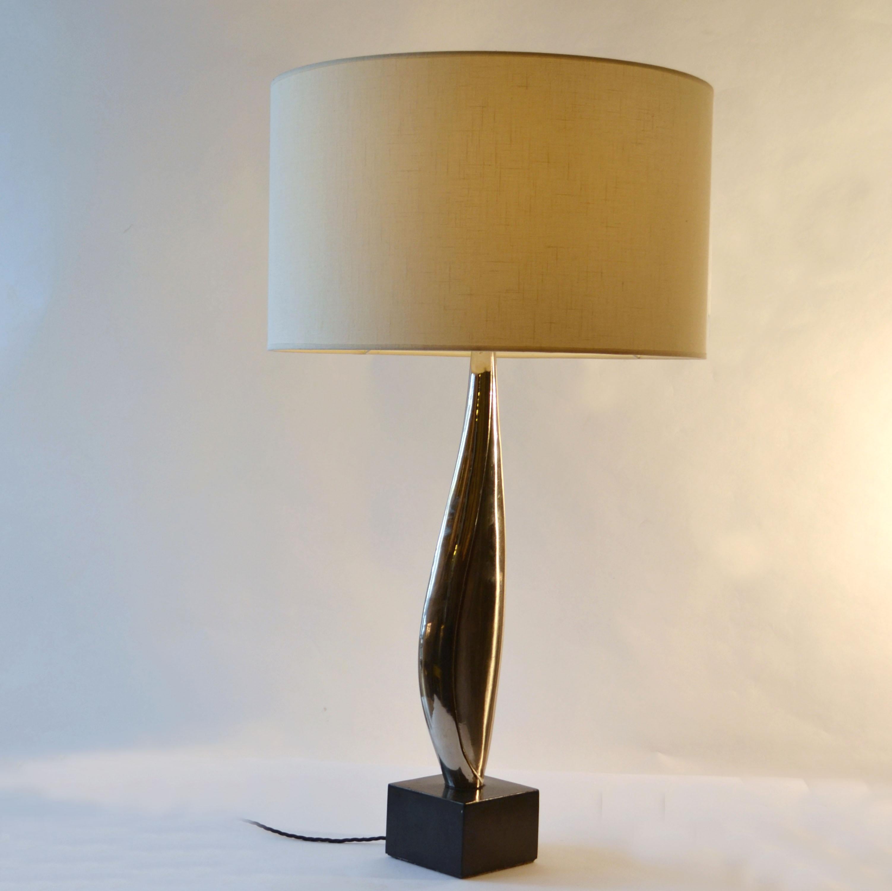 Grande et mince lampe de table des années 1960, de style classique et sculptural, aux lignes fluides et élégantes, caractéristiques de ses fabricants parisiens. La tige est nickelée sur laiton ou bronze. La lampe de table repose sur une base