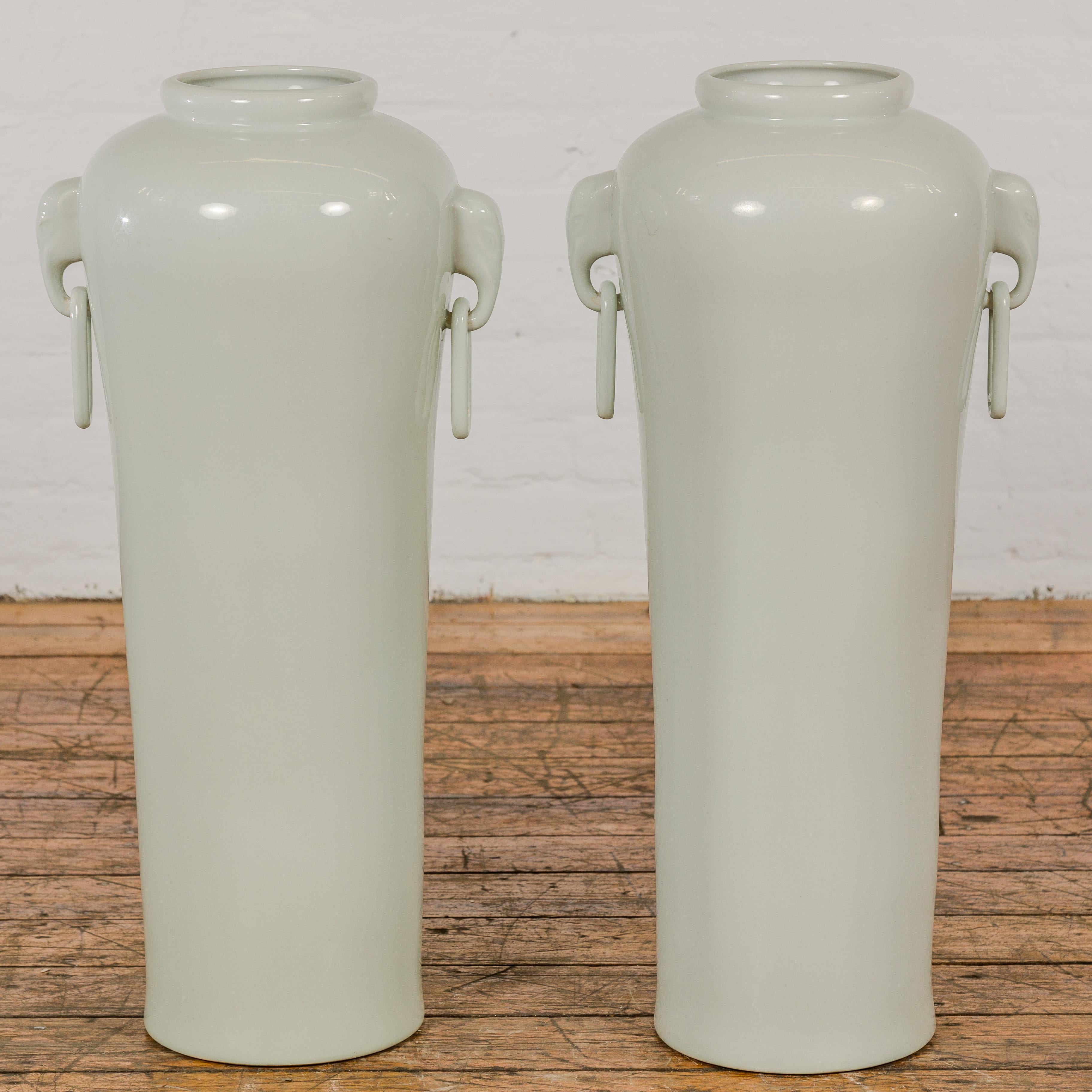 A very near pair of white porcelain tall and slender vintage altar vases with elephant handles, ring pulls and tapering lines. Presenting a near pair of vintage altar vases, these porcelain pieces boast a towering elegance, enriched by their white