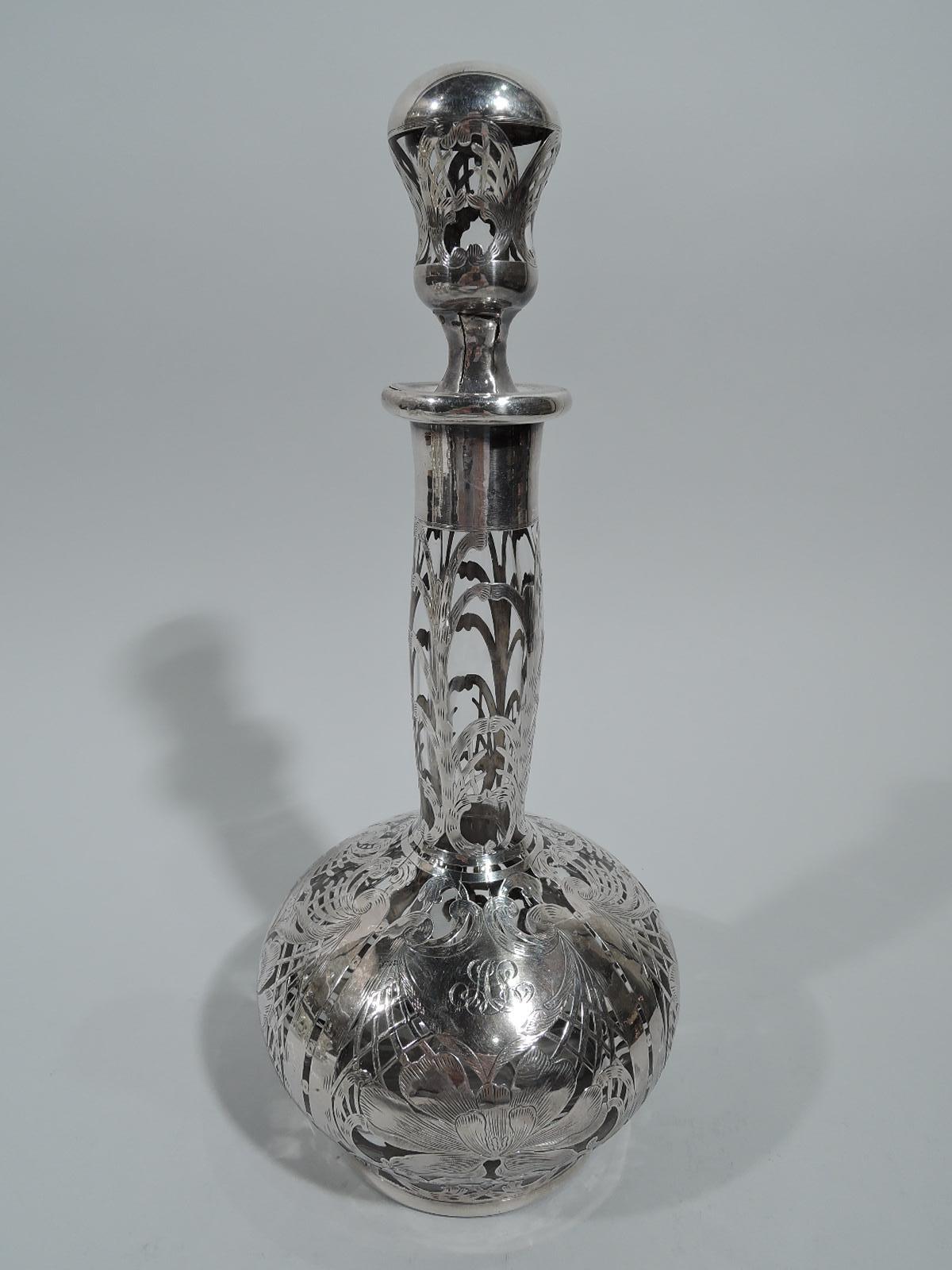Tall turn of the century Art Nouveau glass decanter with engraved silver overlay. Globular bowl with cylindrical neck and everted rim. Stopper concave with faceted neck. Dense overlay. On bowl are flower heads, entwined scrolls, and trellis between