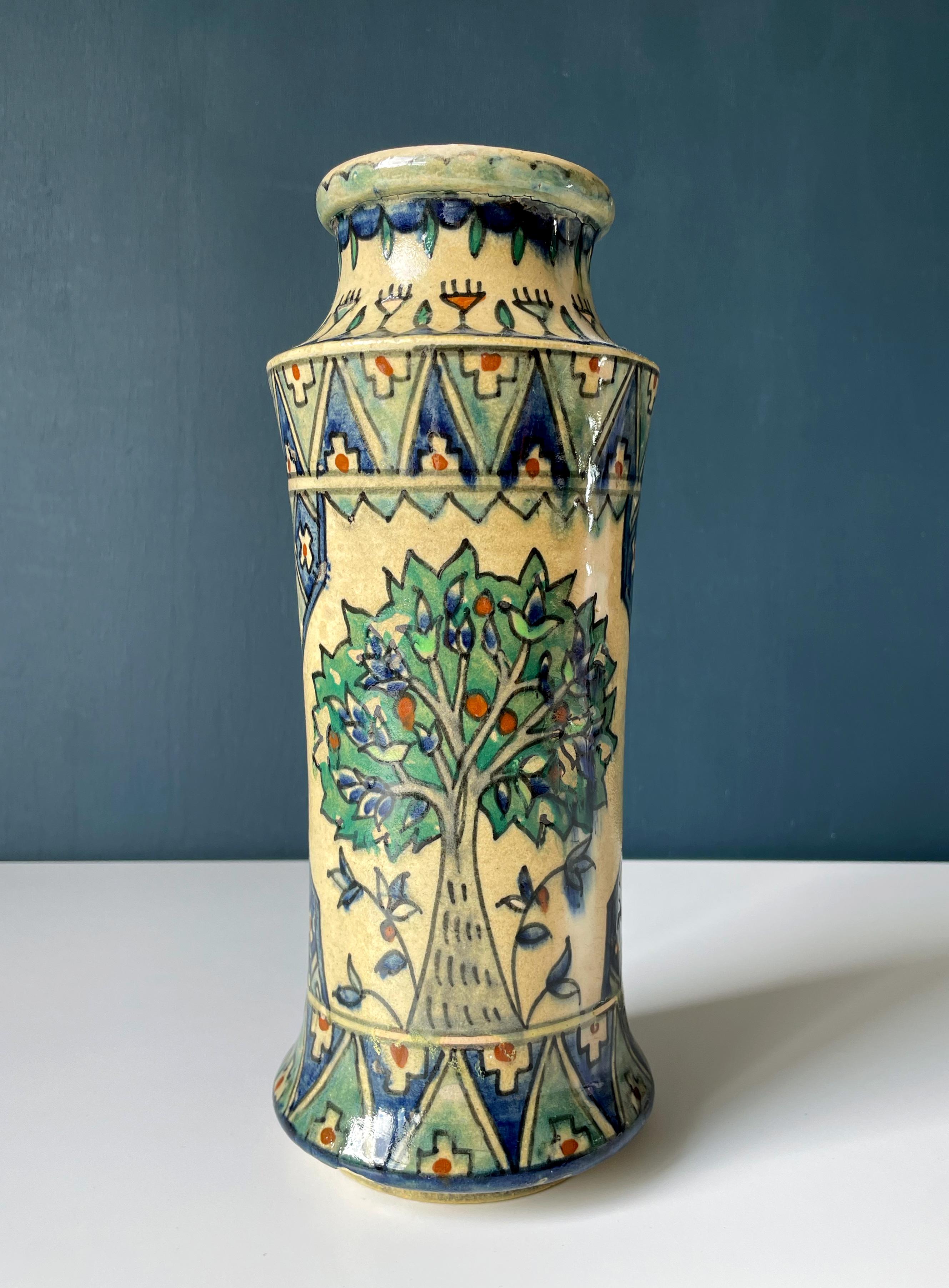 Rare tall and slender early 20th century cylinder shaped Armenian ceramic vase with floral, organic and graphic decorations handpainted in green, blue, red, gray colors on sand colored pottery base under clear glaze. Manufactured by Armenian pottery