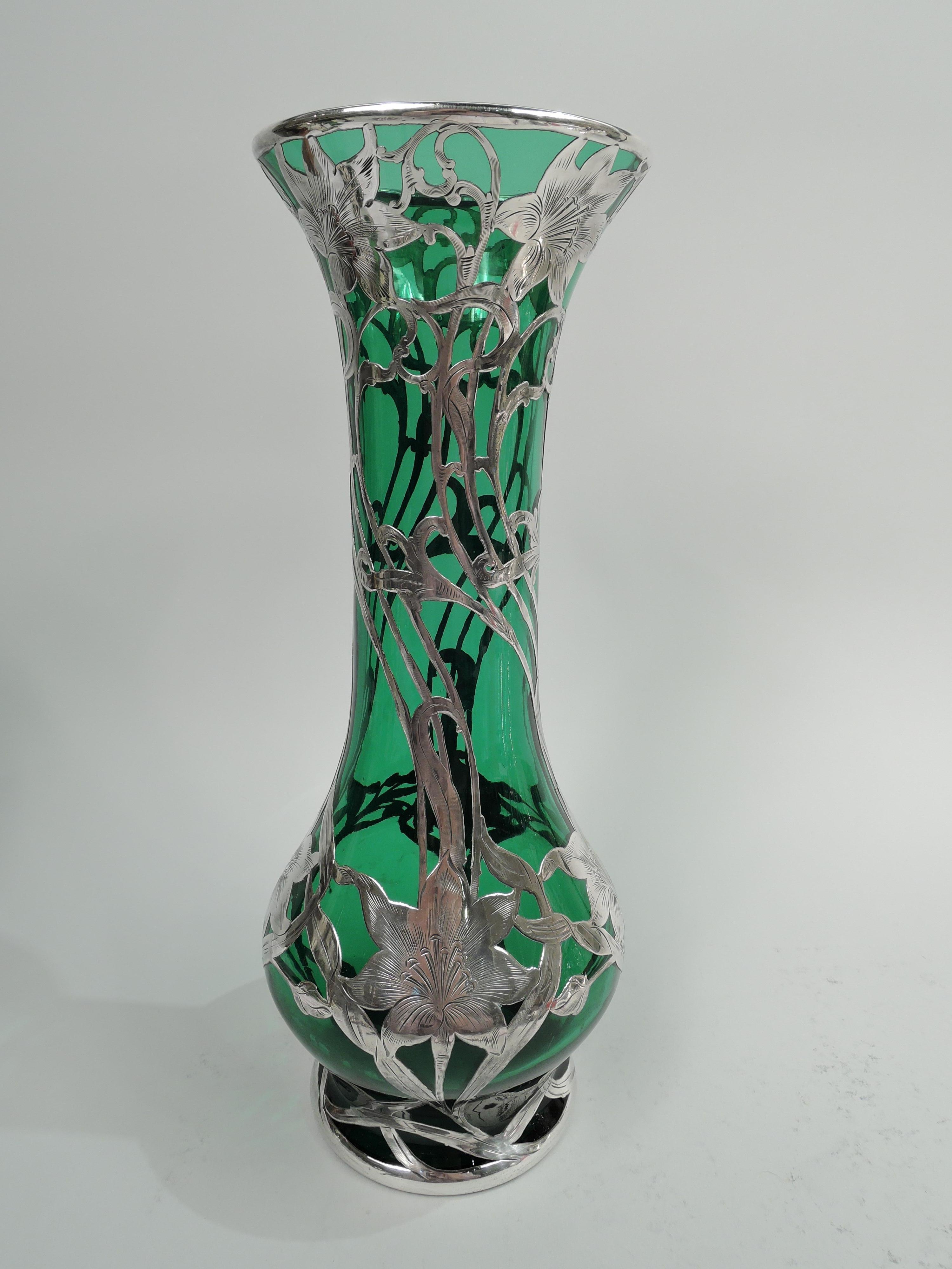 Turn-of-the-century Art Nouveau glass vase with engraved silver overlay. Made by Alvin Corporation in Providence. Tall baluster with flared rim and short foot. Overlay in form twisted tendrils entwined and overlaid with flower heads. Glass is green.