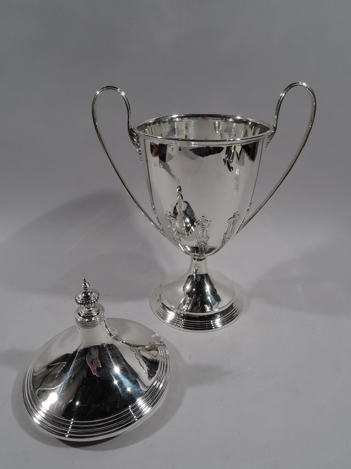 George V sterling silver covered urn. Made by Alexander Clark Co. Ltd in Birmingham in 1926. Oval bowl with leaf-mounted high-looping handles; short support flowing into raised foot. Cover domed with lobed vase finial. Bowl base has applied and