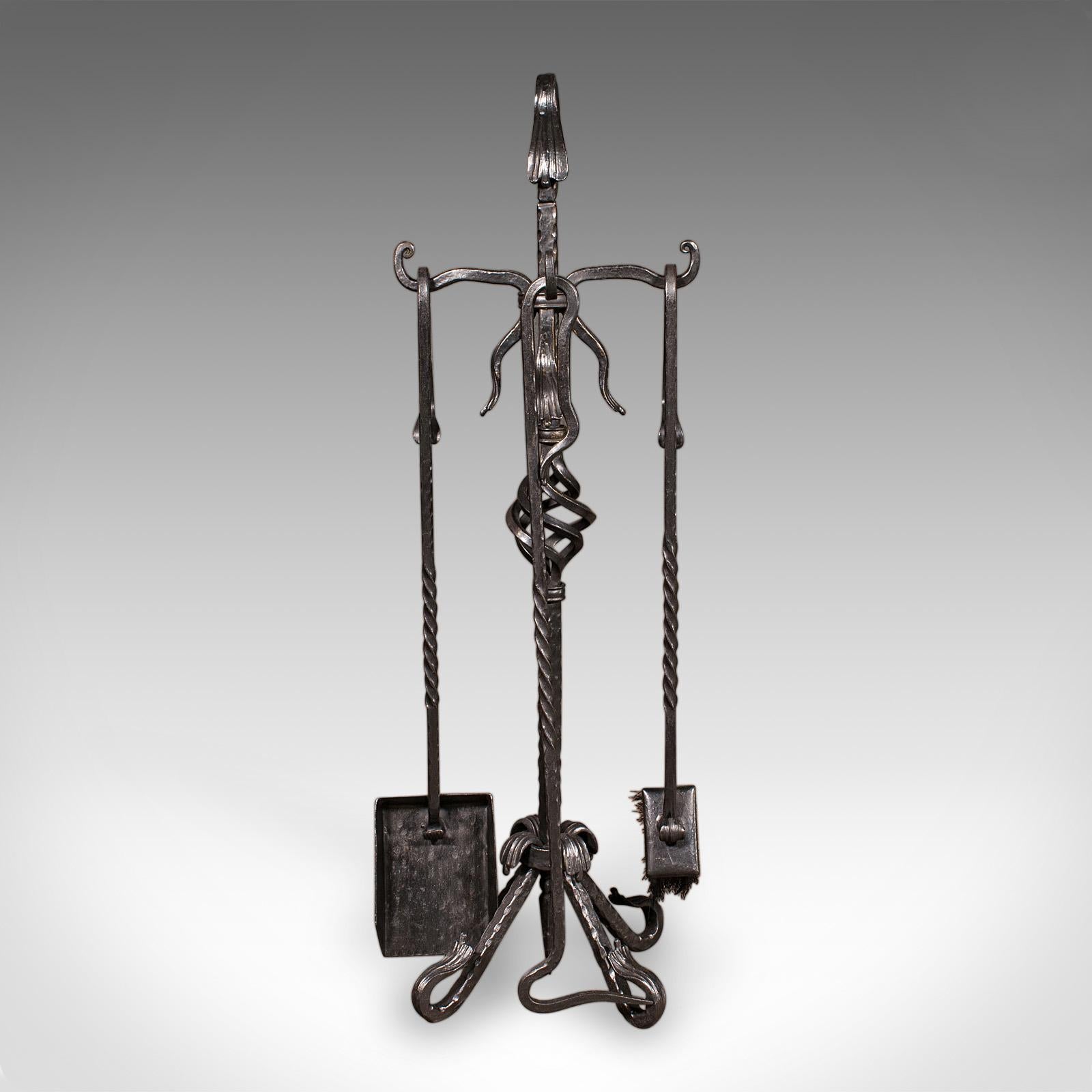 This is a tall antique fireside companion. An English, wrought iron set of fire tools presented upon an ornate stand, dating to the Edwardian period, circa 1910. Neatly arranged and expertly crafted, this fireside set offers enduring utility and