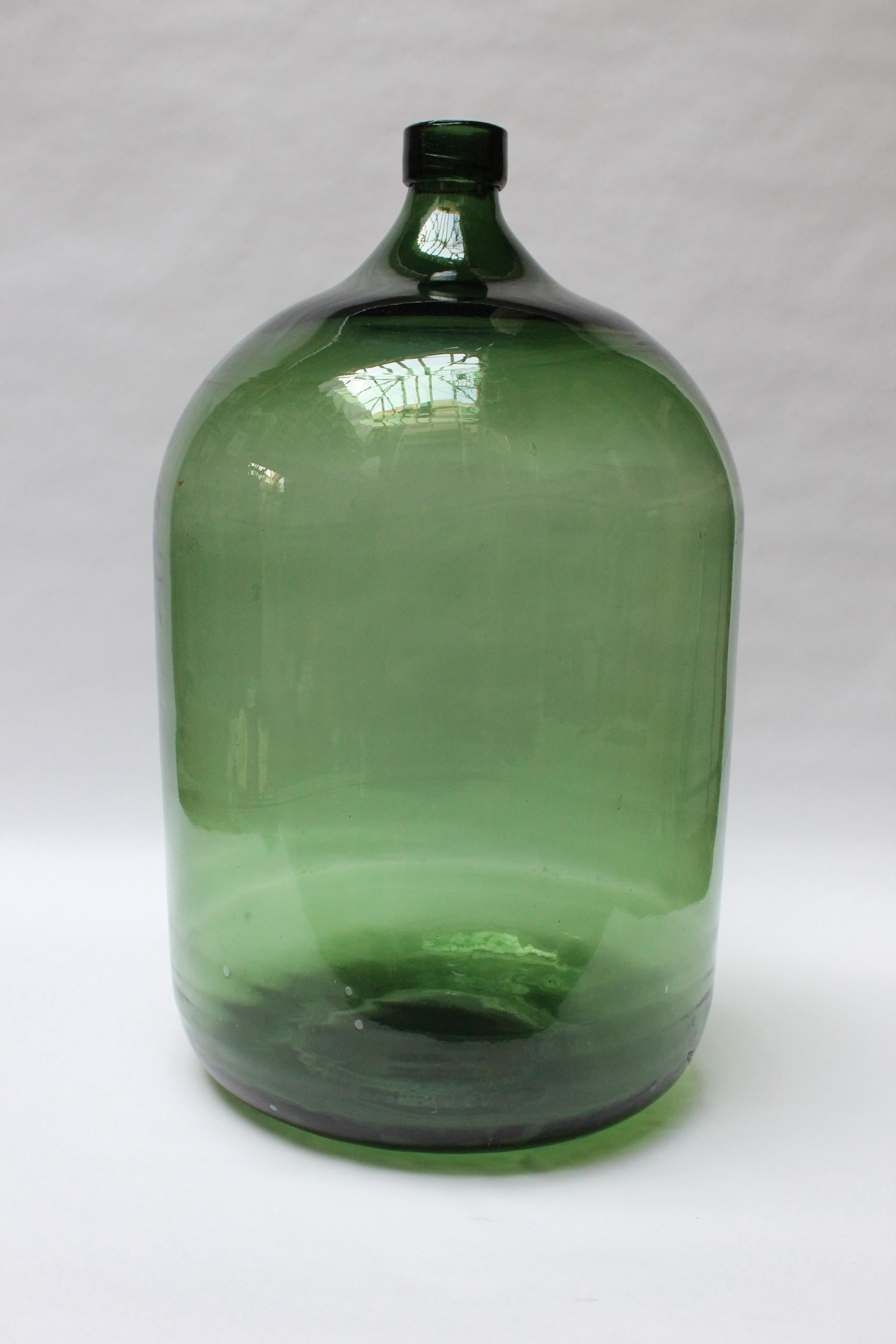 French Demijohn / Carboy originally used for transporting wine (ca. late 19th Century, France). Composed of free-blown emerald glass exhibiting trapped air bubbles within the glass itself. Striking color and unique form with a shorter lip and more