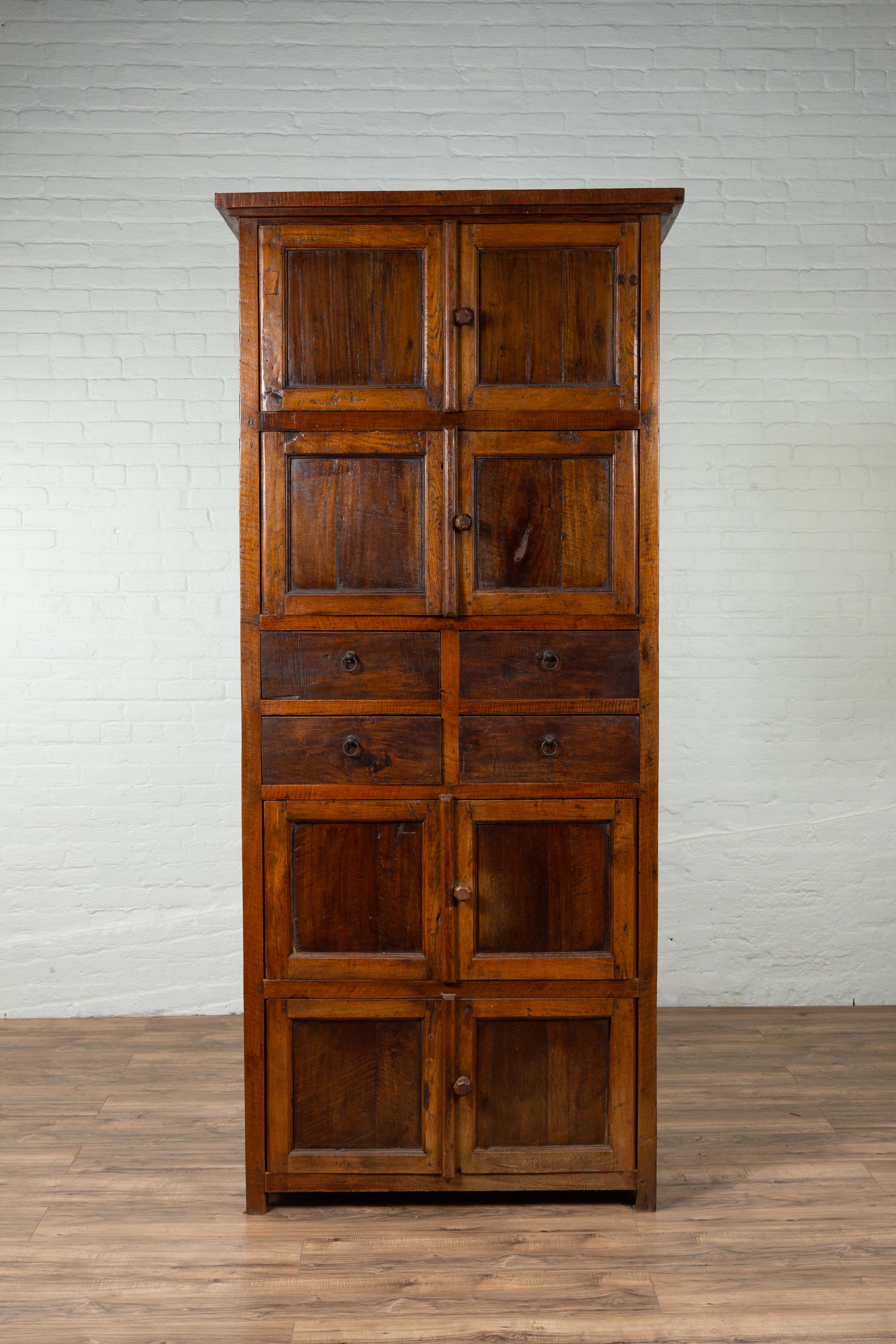 A tall antique Indonesian teak wood cabinet from Java with four sets of double doors and four drawers. Born on the island of Java during the early years of the 20th century, this tall and narrow cabinet features a lovely brown patina. Topped with an