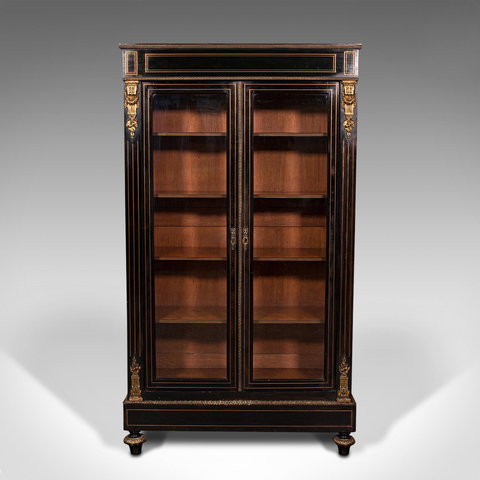 This is a tall antique vitrine cabinet. An English, ebonised mahogany display case or glazed bookcase, dating to the Regency period, circa 1830.

Beautifully appointed cabinet of superb craftsmanship
Displays a desirable aged patina and in good