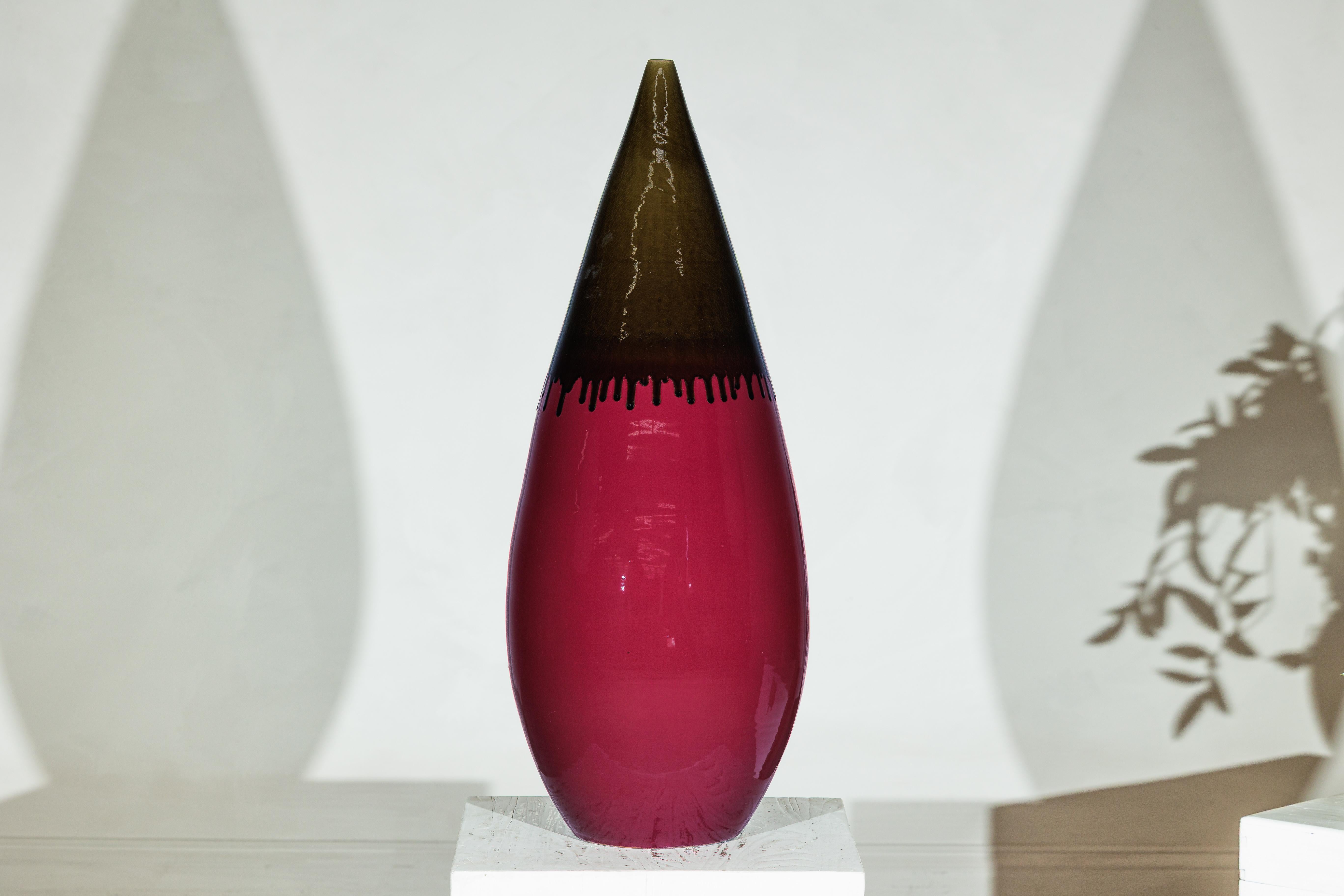 Diese hohe, handwerklich gefertigte Keramikvase bietet mit ihrer langgestreckten, tropfenförmigen Silhouette und der raffinierten Oberflächenbehandlung ein auffälliges Zusammenspiel von Farbe und Form. Das Gefäß ist mit einer reichhaltigen