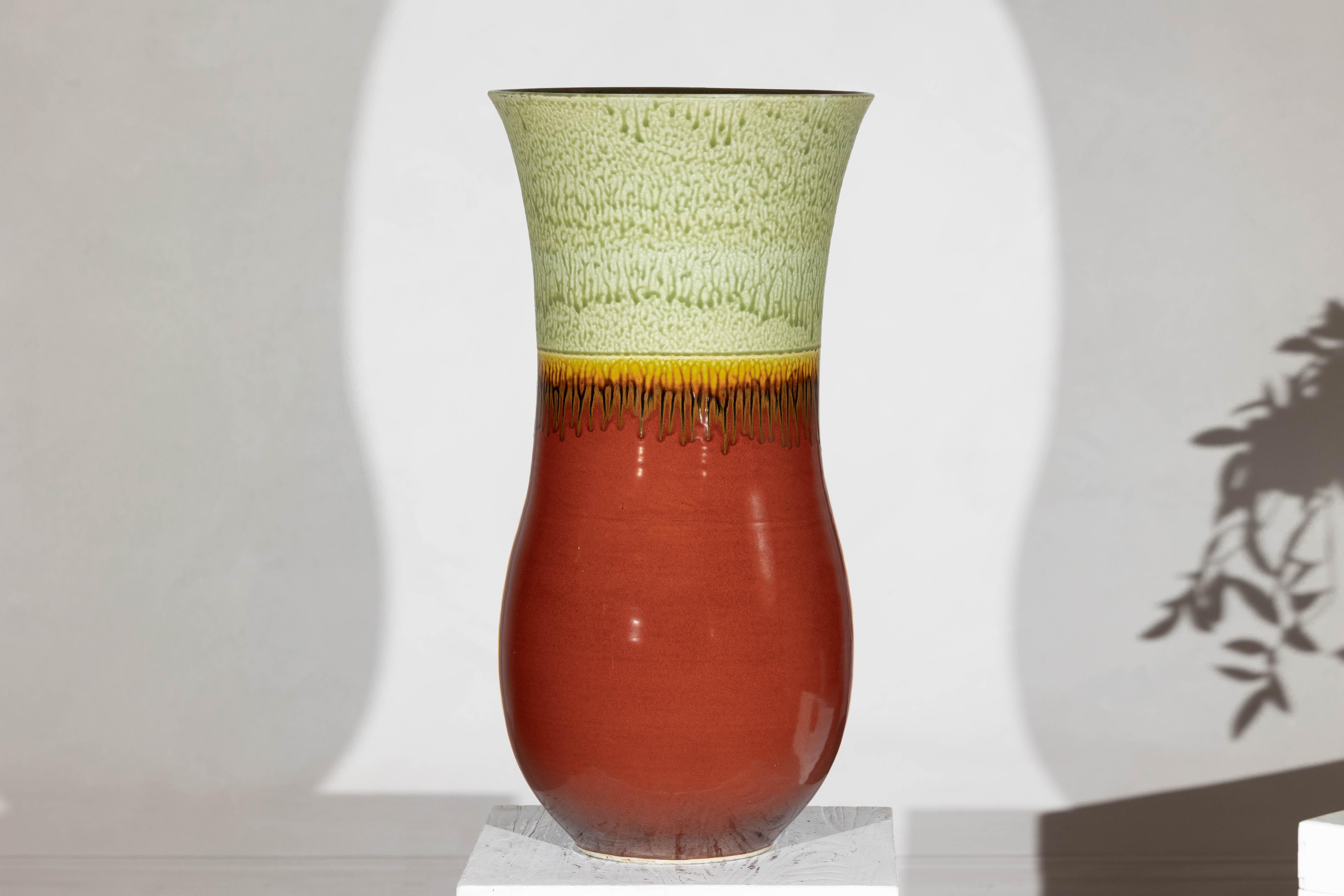 Questo vaso in ceramica fatto a mano, imponente sia nella scala che nel colore, offre un equilibrio sorprendente tra la consistenza della terra e la finitura vibrante. La sua silhouette allungata si svasa con grazia sul bordo, dove uno smalto