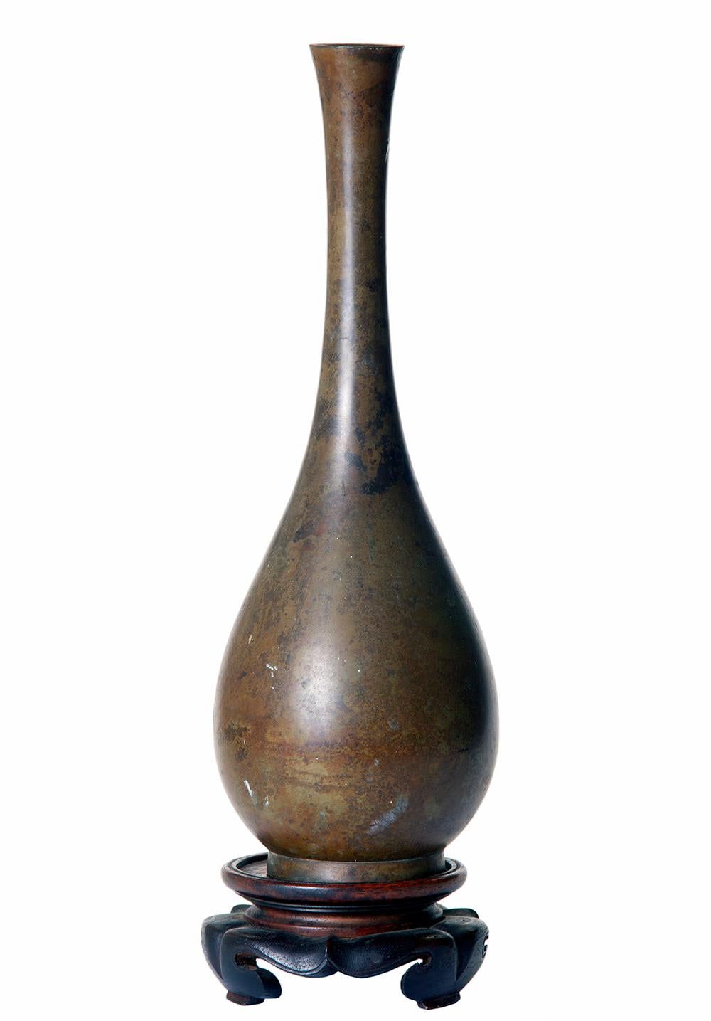 Tall Asian bronze bud vase with a smooth mottled hand.
The slender vase sits on a hand carved rosewood stand.