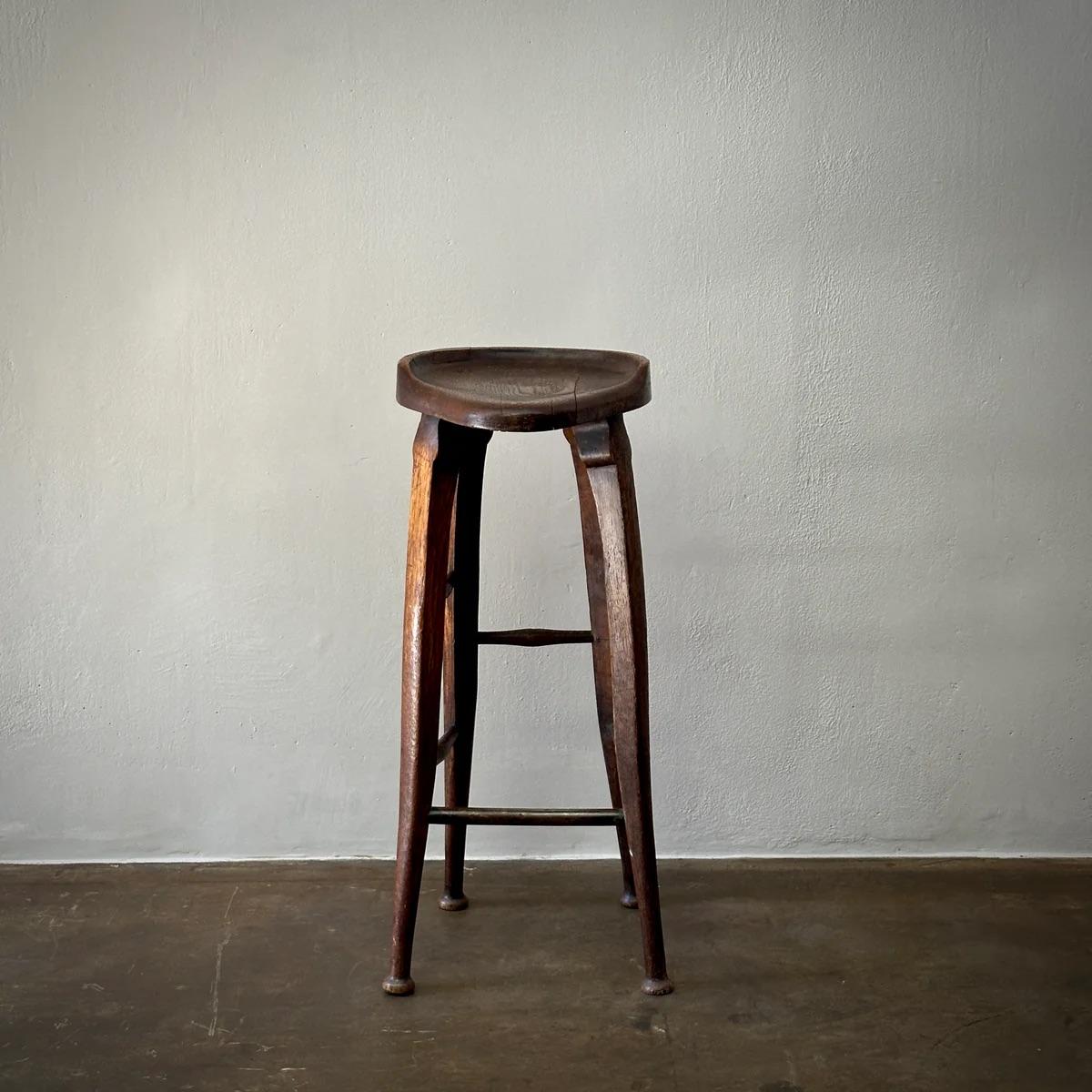 This English mahogany bar stool exemplifies traditional craftsmanship with its slim, tall profile and gracefully tapered legs, finished with petite bun feet. The stool's mahogany construction ensures durability while maintaining a delicate