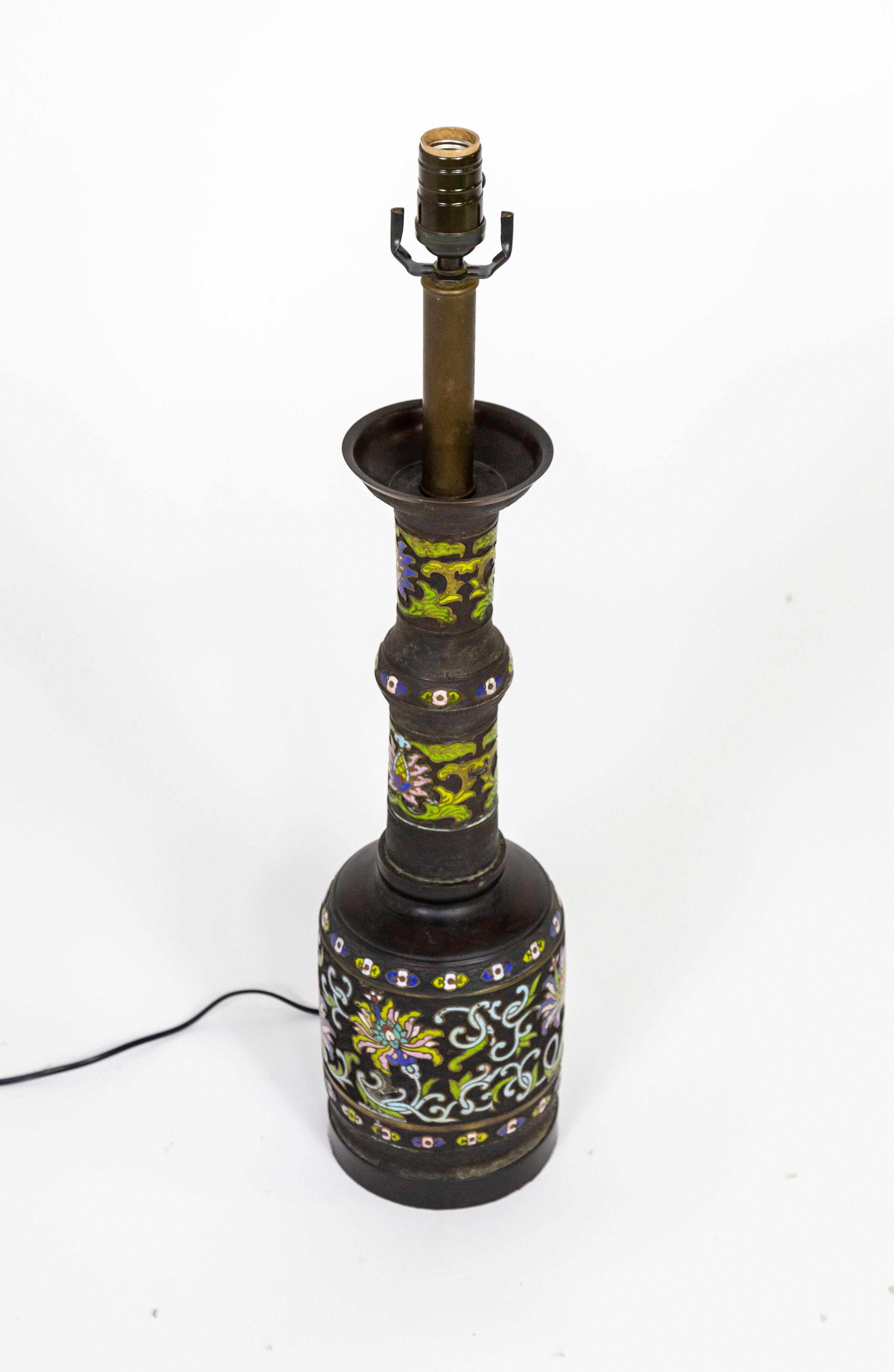An early 20th century, black patinated, cast bronze and champleve enamel lamp; in an elongated shape with intricate greek key surface texture and floral motif. Champleve is a technique that creates recesses in metal by etching or casting and then