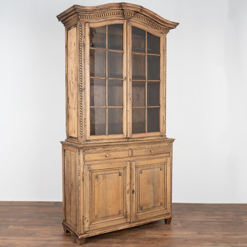 This striking tall oak cabinet has been giving a bleached finish, adding a fresh look to the French country style. 
The upper glass doors allow for wonderful display of the guns held within; newer gun rack installed and stained to compliment the