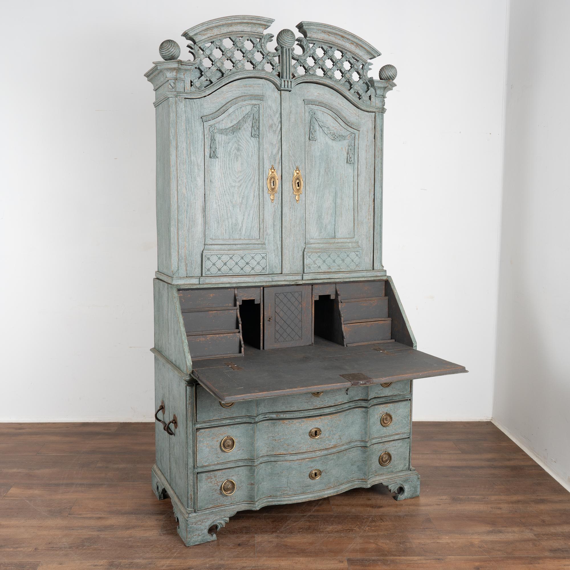 This striking oak secretary is an elegant statement piece crowned with an elaborate latticework bonnet and finials.
The entire secretary has been given a professional custom layered blue painted finish which has been gently distressed to reveal the