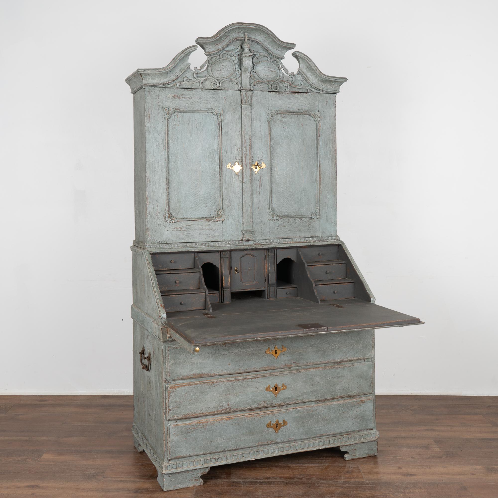 This striking oak secretary is an elegant statement piece crowned with an elaborate carved pediment.
The entire secretary has been given a professional custom layered blue painted finish which has been gently distressed to reveal the original oak