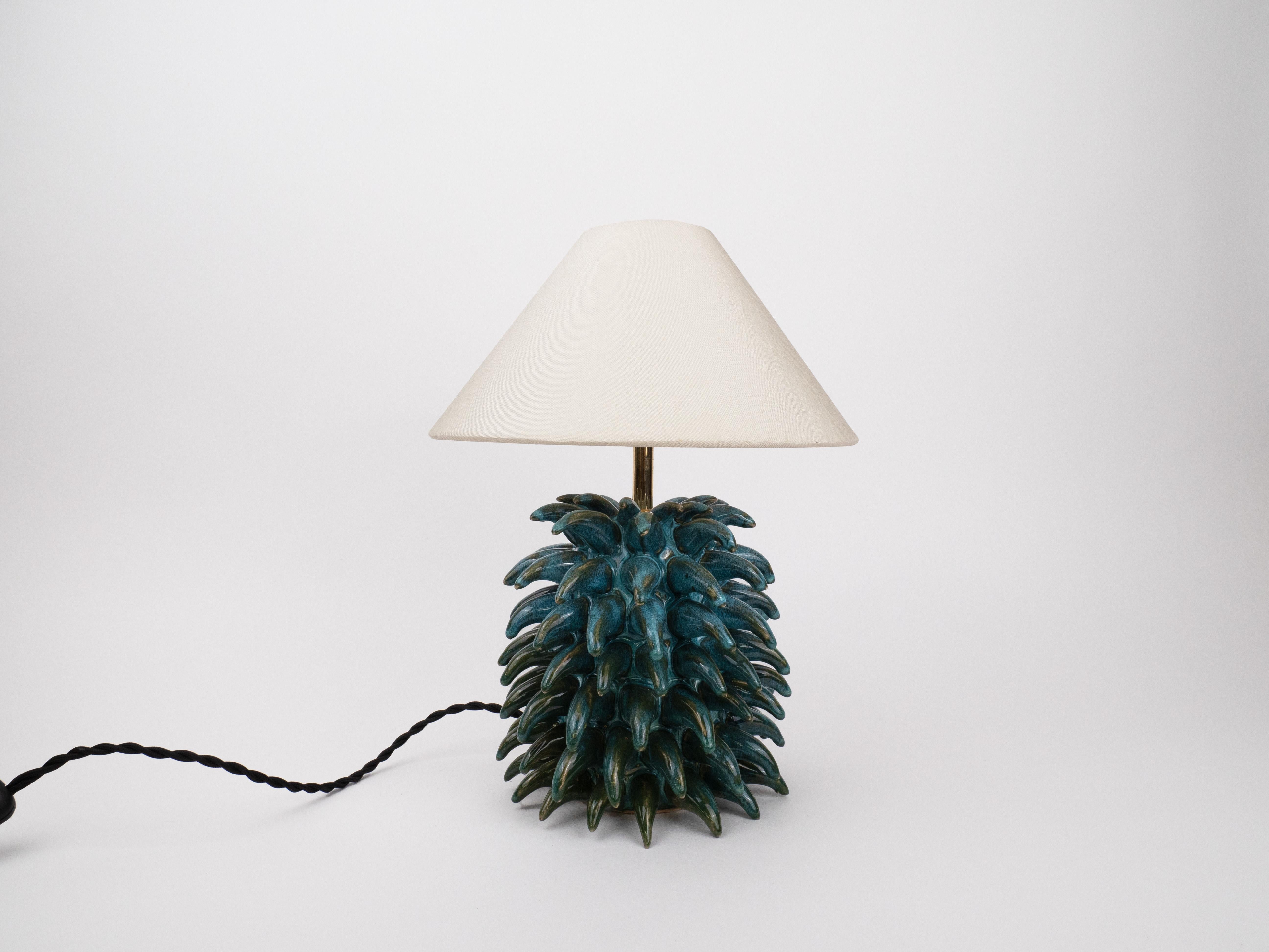 A little lamp with a lot of personality! This handmade ceramic beauty features a deep blue-green glossy base with a delightful spiky texture, bringing a bold yet charming touch to any space. Topped with a classic fabric shade, it gives off a warm,